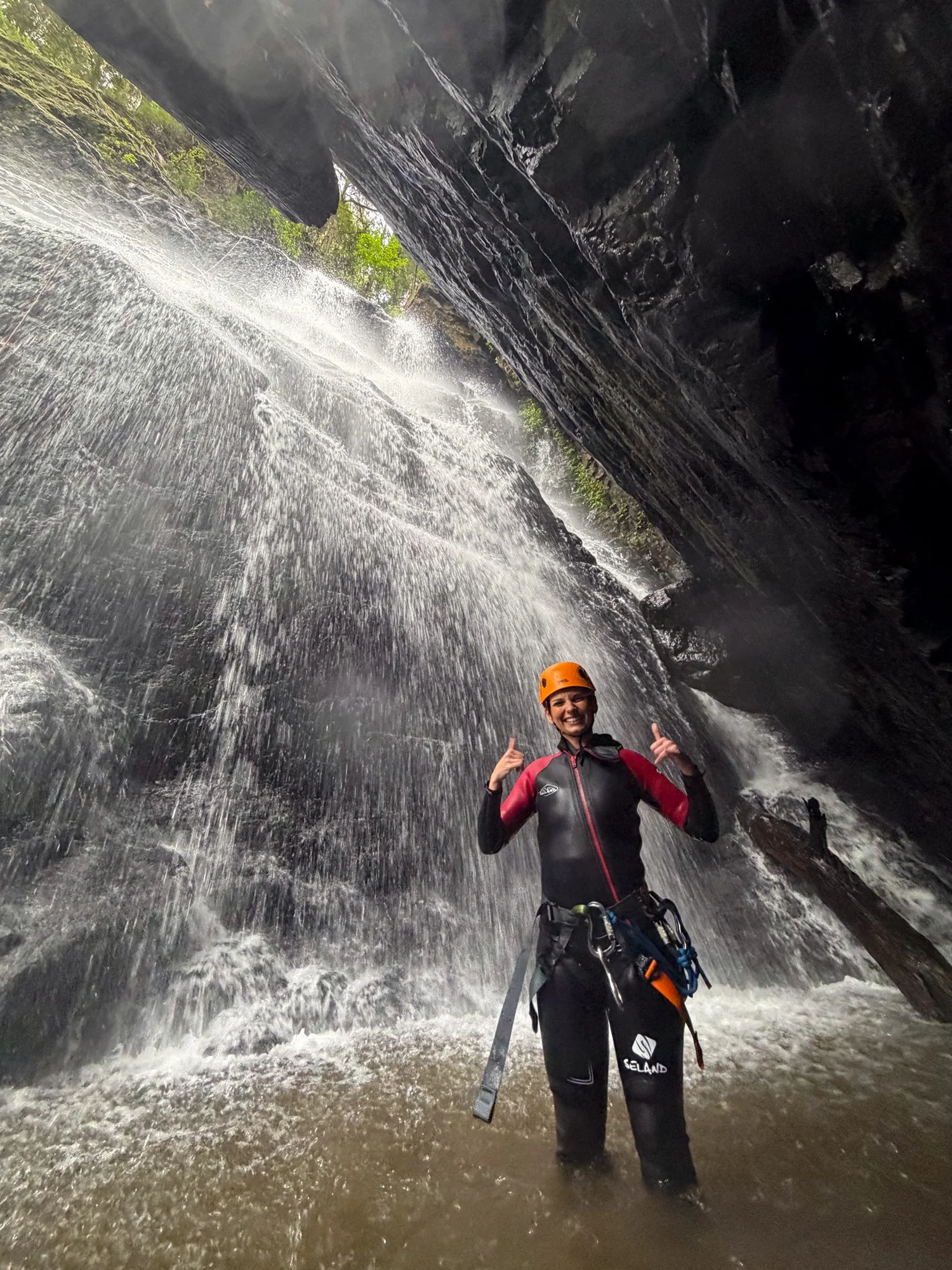 A smiling canyoner enjoying the spray beneath a Coffs Coast waterfall