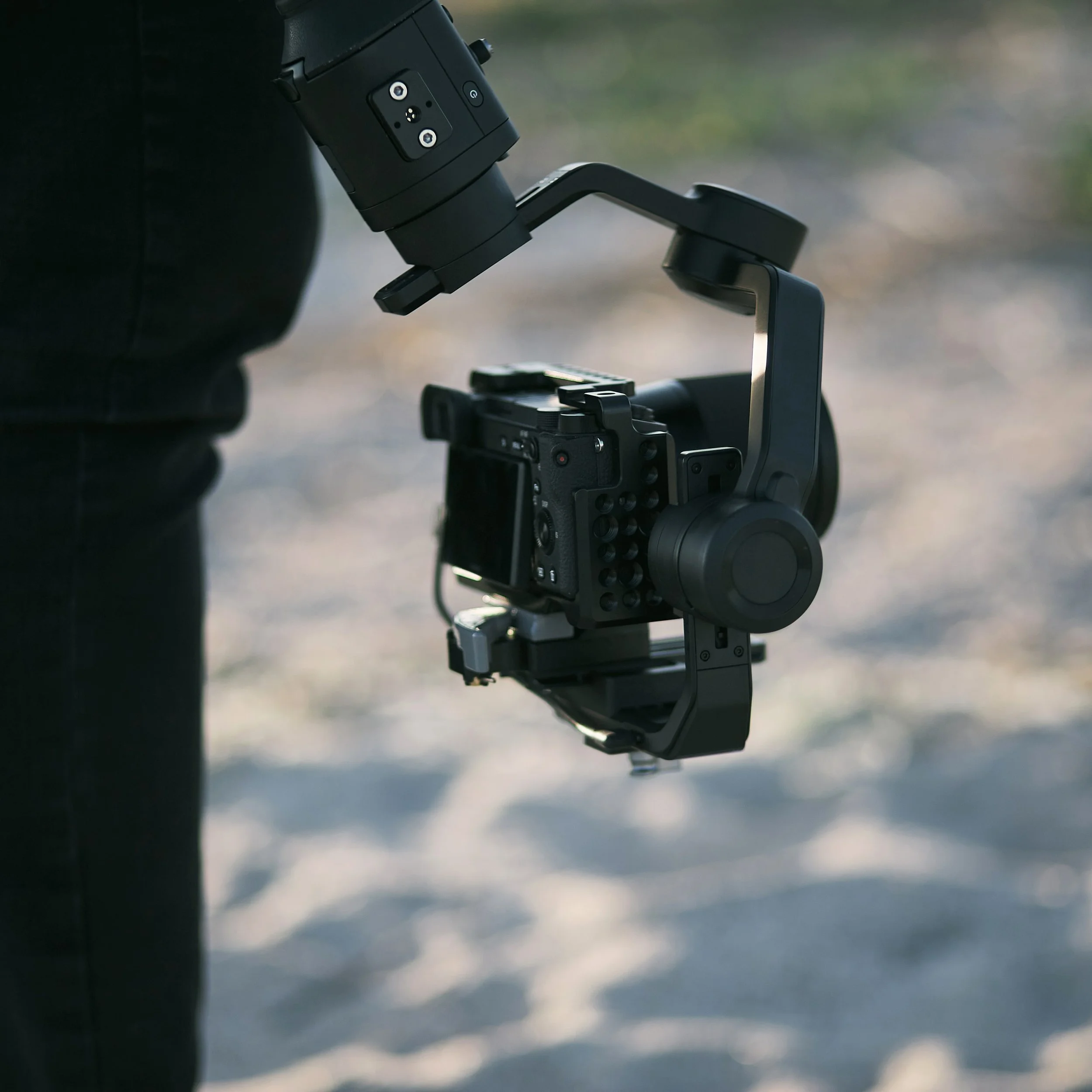Close-up of a camera stabilizer or gimbal with a mounted camera in an outdoor setting, with a blurred background.