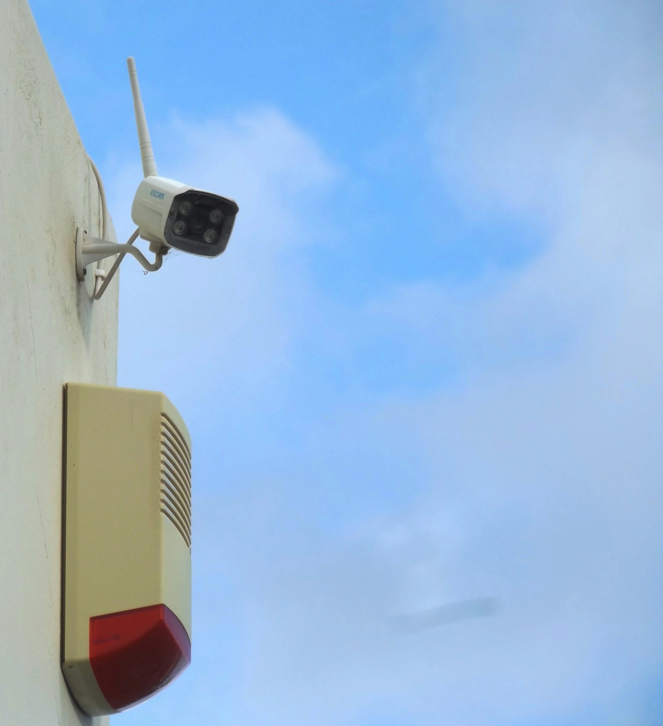 CCTV security camera installed on the top corner of a building wall with a blue sky in the background.