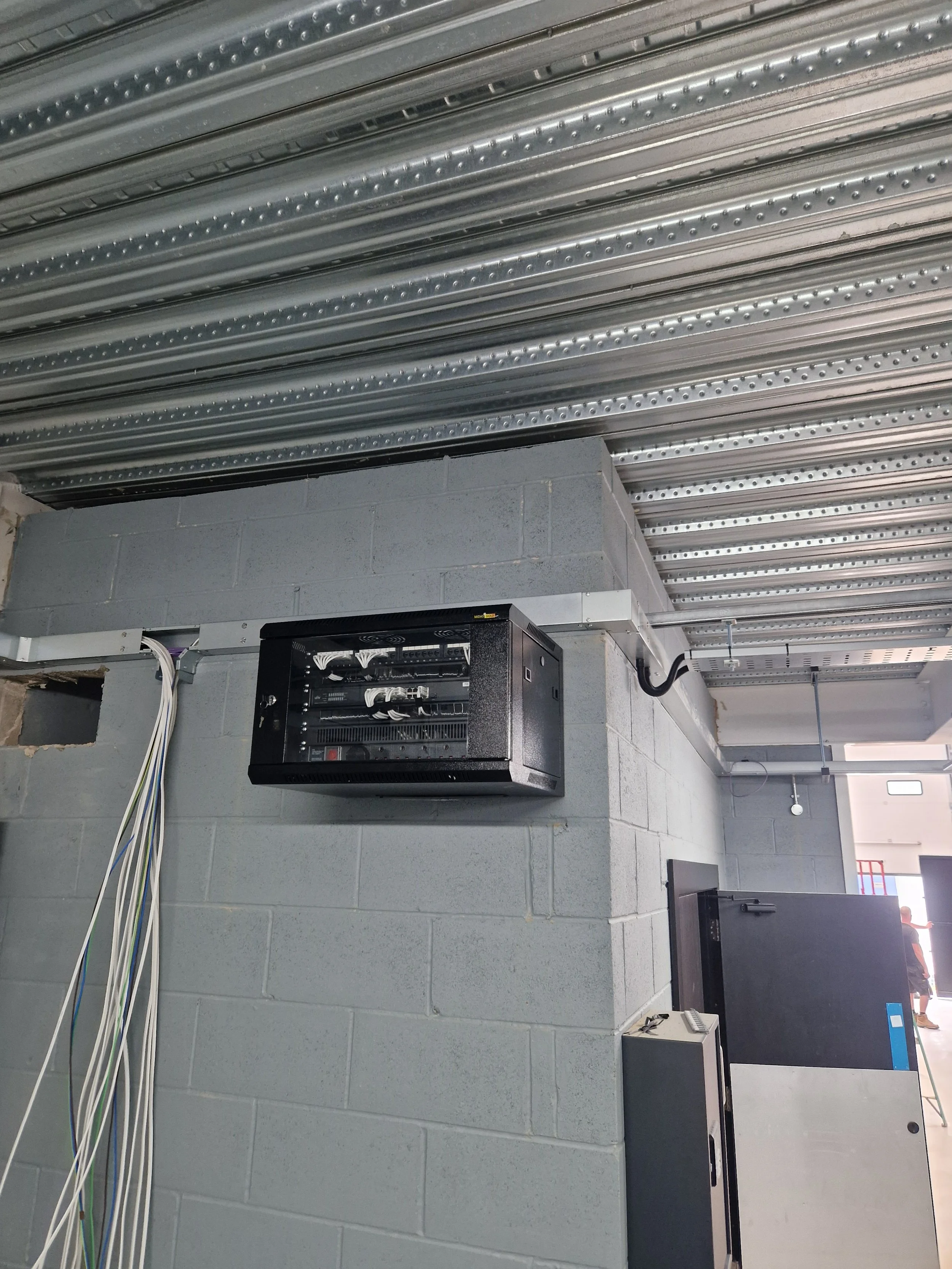 Image of a network server rack mounted on a concrete wall, with multiple cables connected to the front panel.