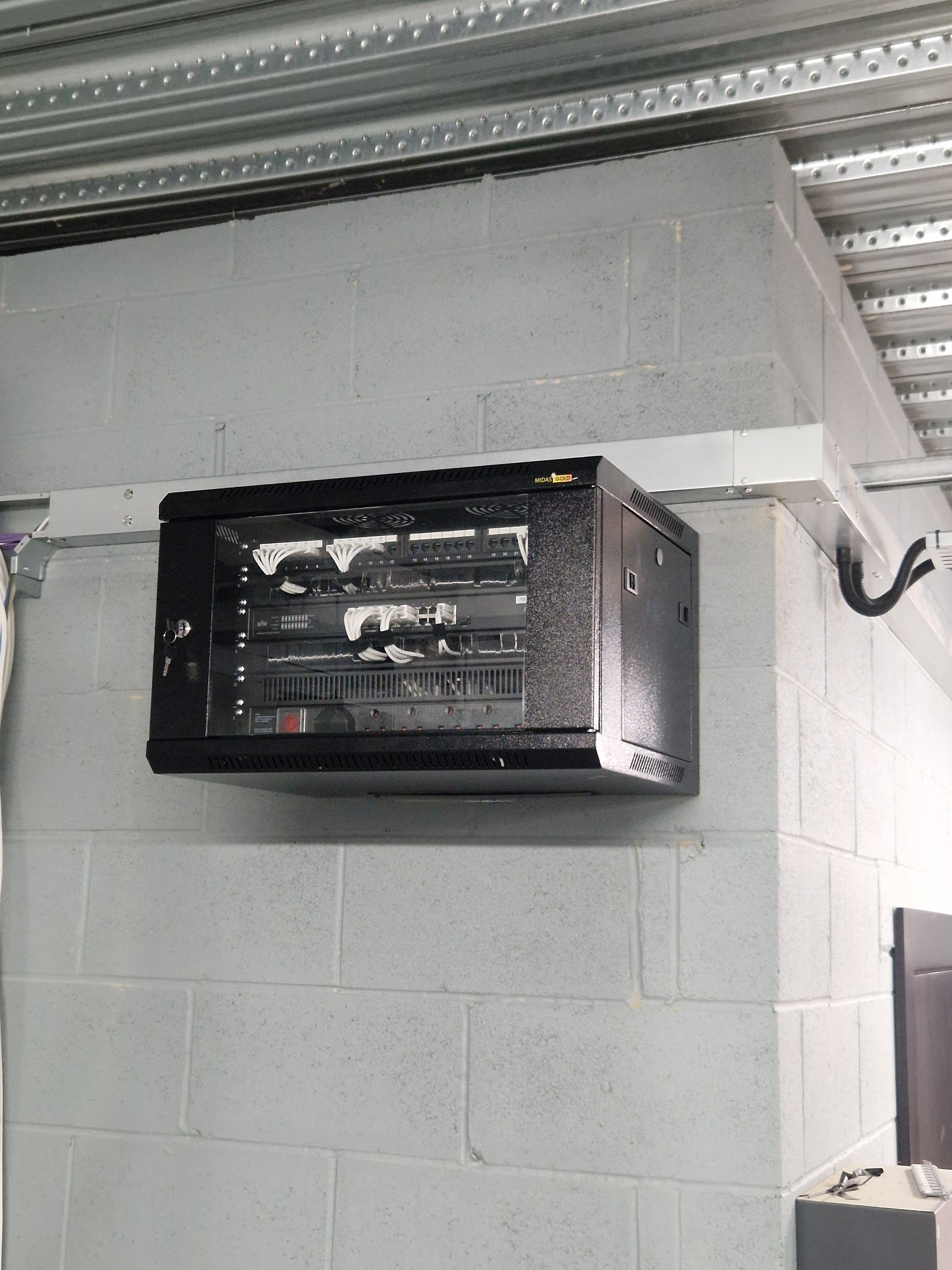 An electrical panel mounted on a gray cinder block wall in an industrial or technical setting.