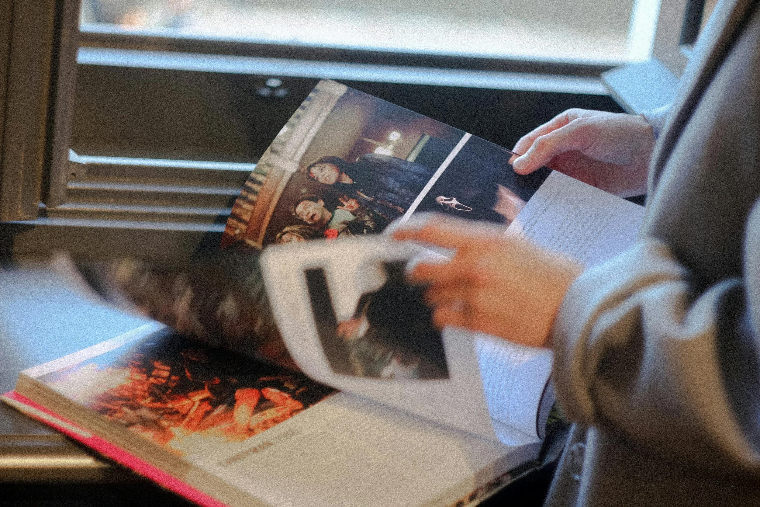 Person holding a magazine or booklet featuring images of people, possibly band members or performers, in a setting with books and other materials nearby.