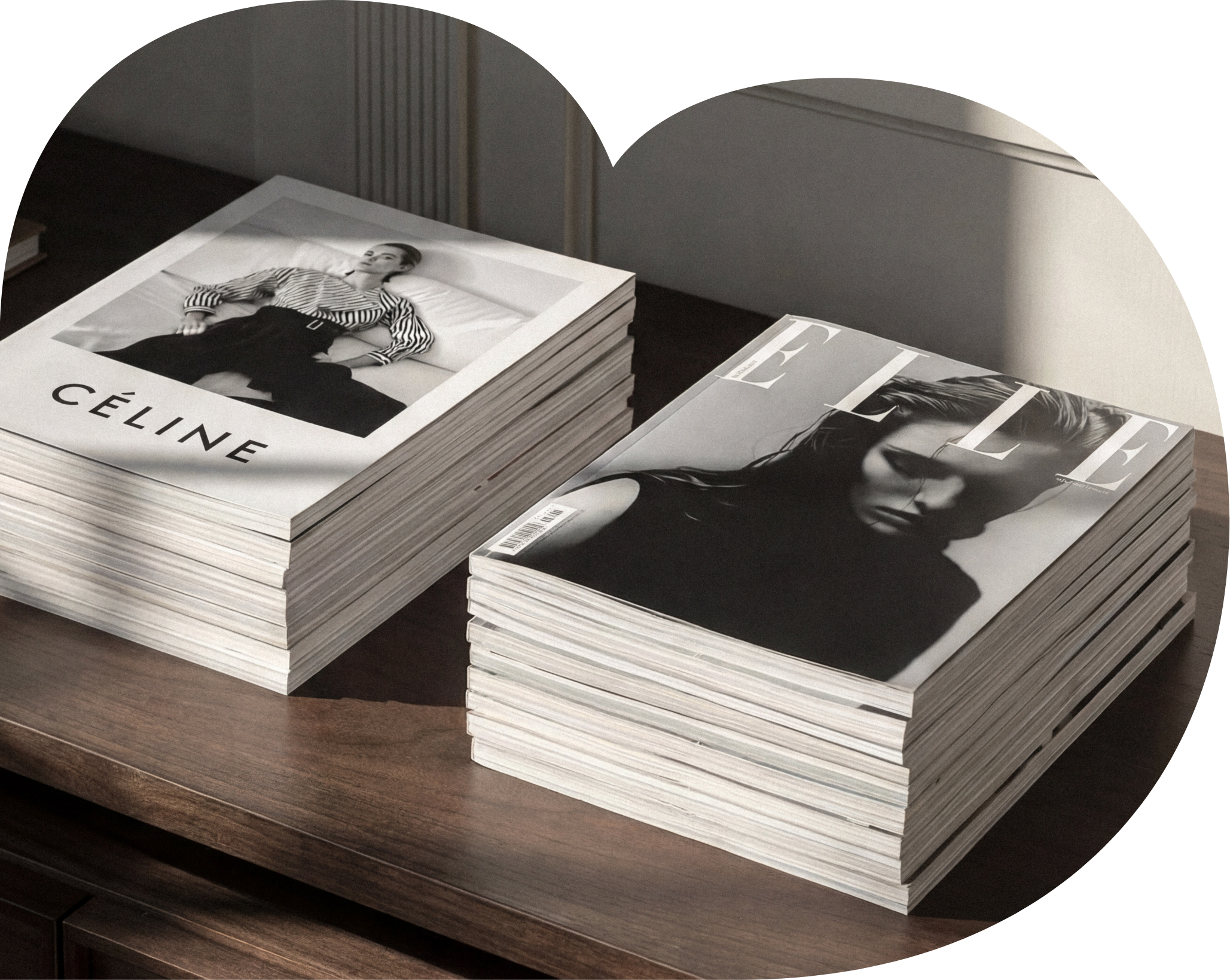 Stack of magazines on a wooden table, featuring a black and white cover photo of a woman wearing a striped shirt.