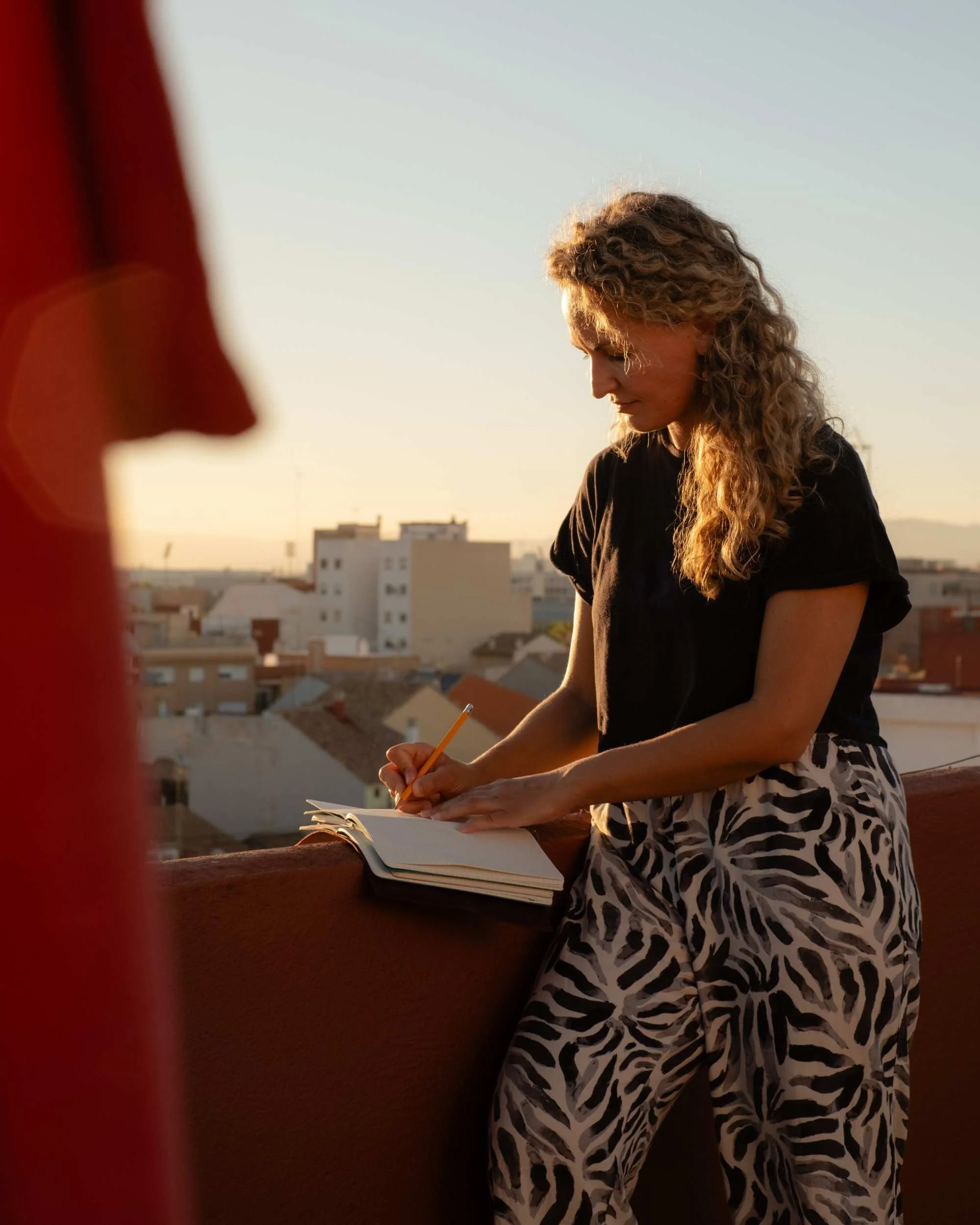 Johanna Czekalla sitzt auf einer Dachterrasse und schreibt in ihr Notizbuch