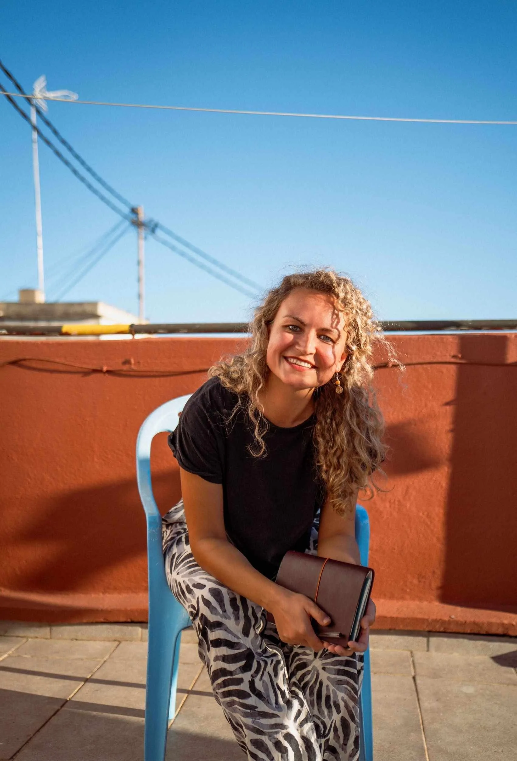 Johanna Czekalla sitzt auf einer Dachterrasse mit einem Notizbuch und lächelt in die Kamera.