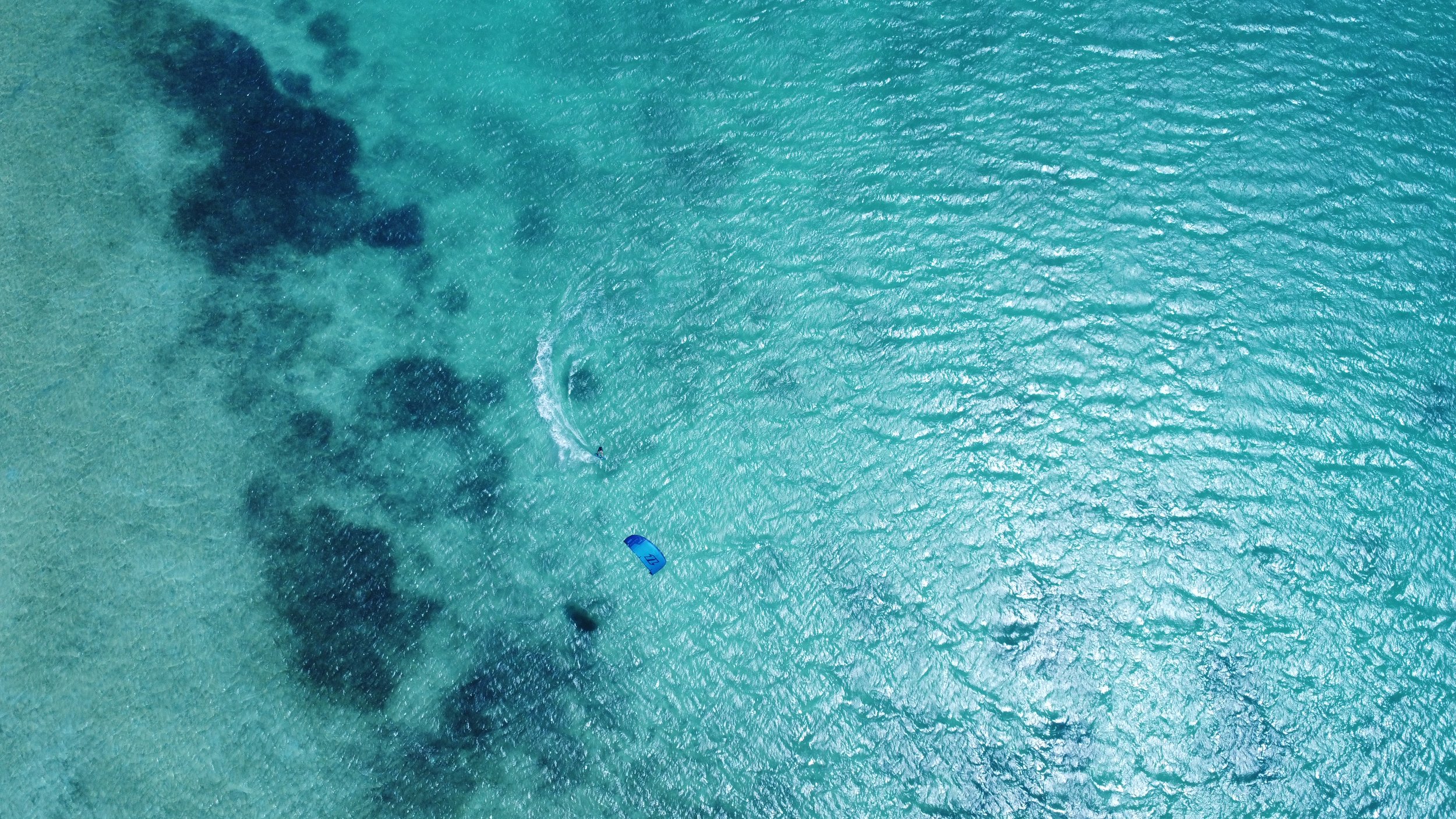 An aerial view of clear turquoise ocean water with a small boat and a wake trail from the boat.