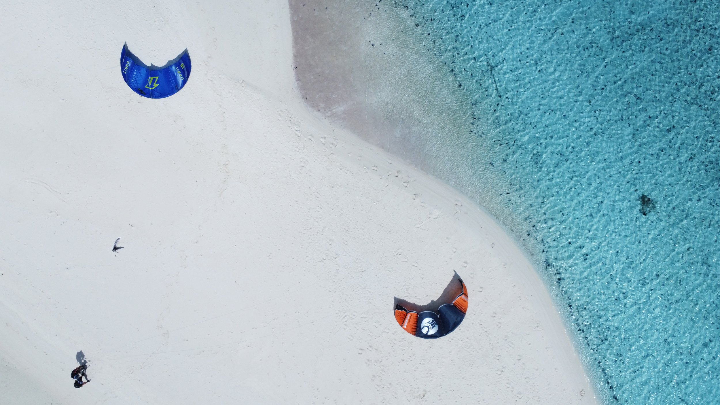 Photo taken from a first-person perspective showing a snow-covered landscape with a partially visible kiteboarder, a kite, and a body of water.