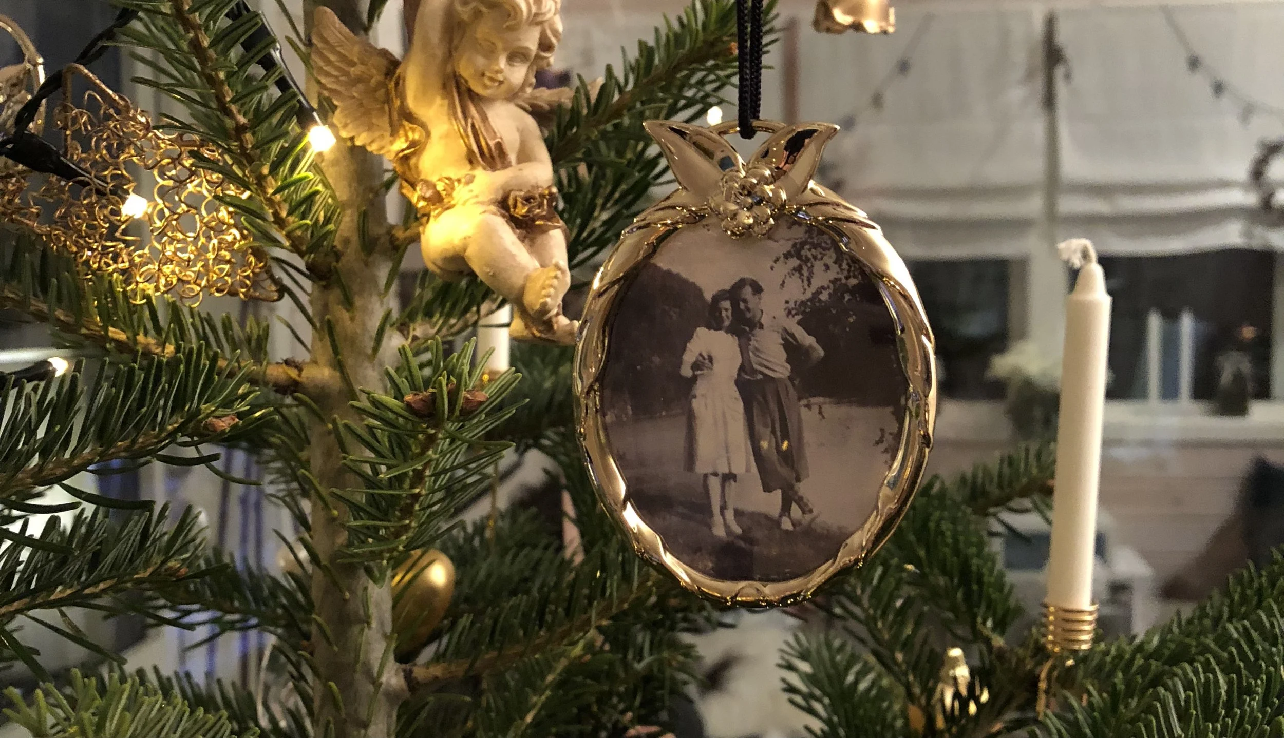 Festiv ornaments på juletreten, inkludert en dekorasjon med eldre bilde av et par, en nissefigur, og lys.