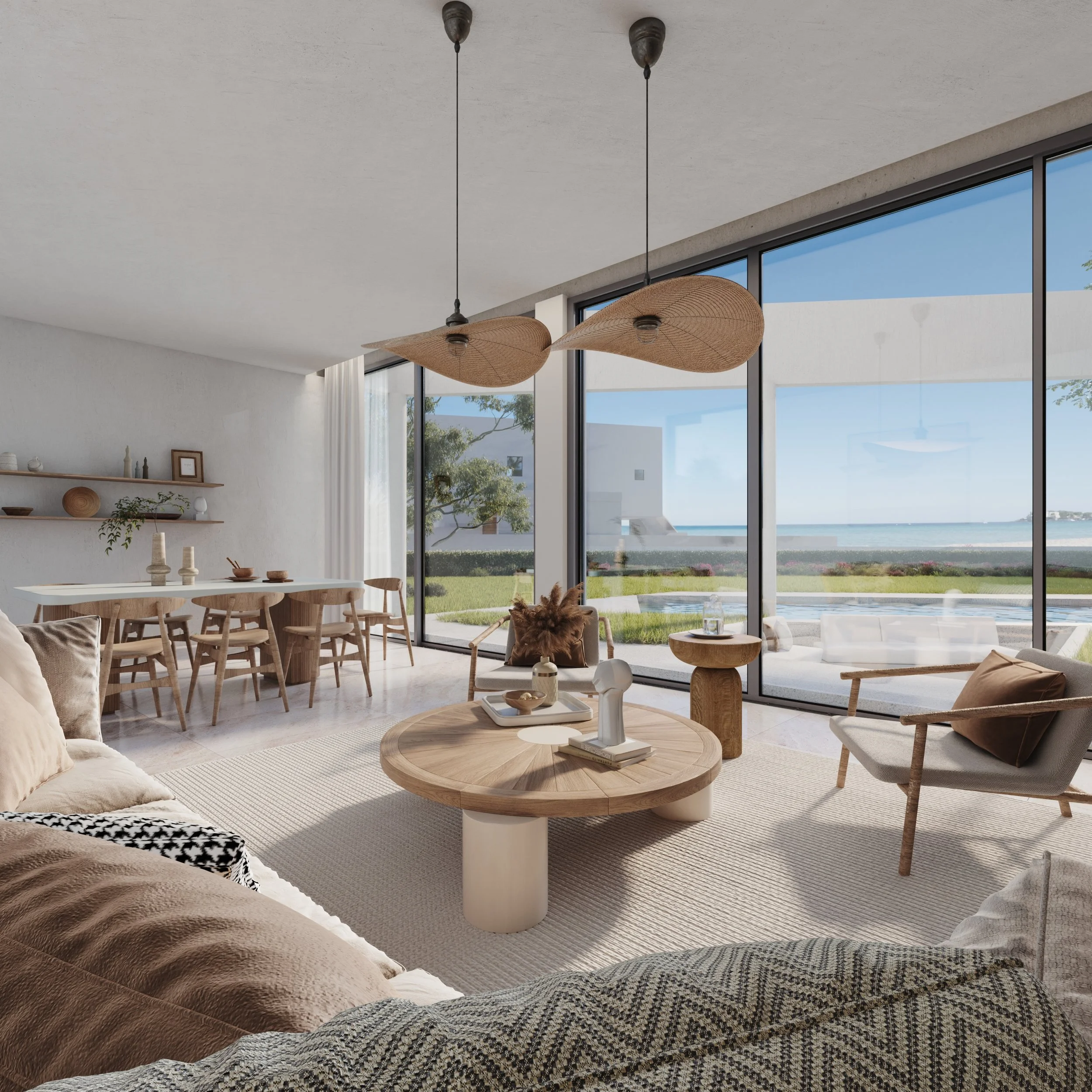 Modern living room with beige sectional sofa, patterned throw blankets, and a round wooden coffee table surrounded by assorted chairs. Large floor-to-ceiling windows showing an outdoor view of grass, trees, and a body of water, with two pendant lights hanging from the ceiling.