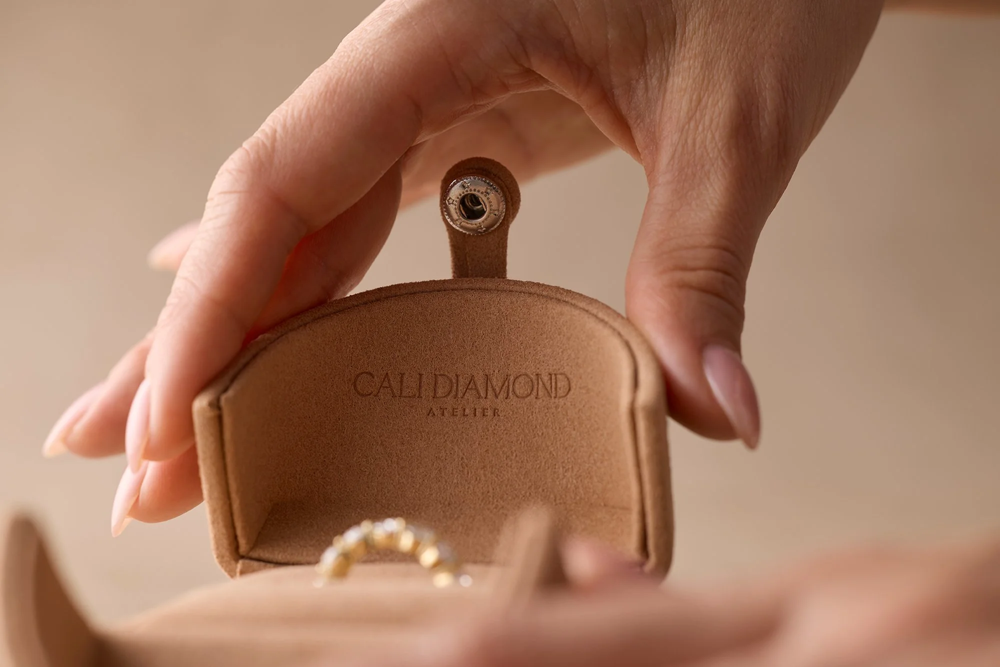 Close-up of a person holding a tan leather cardholder with a ring display inside, with the text 'CAL DIAMOND ATELIER' embossed on the front.