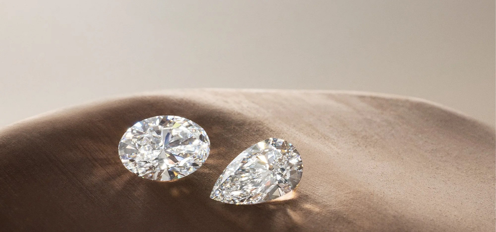 Close-up of two sparkling diamonds resting on a soft, beige fabric surface.