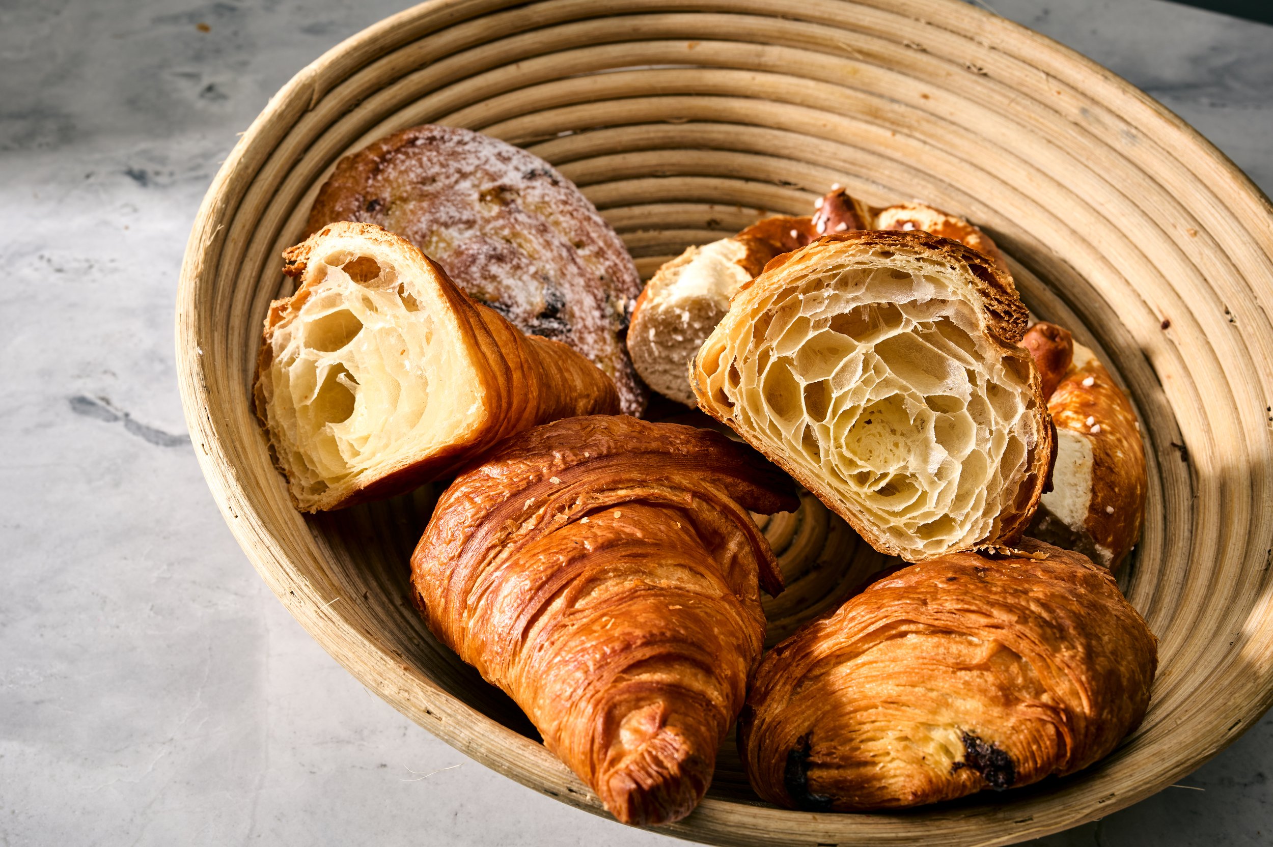 Verschiedene Croissants und Gebäck in einem runden Korb auf einem grauen Tisch
