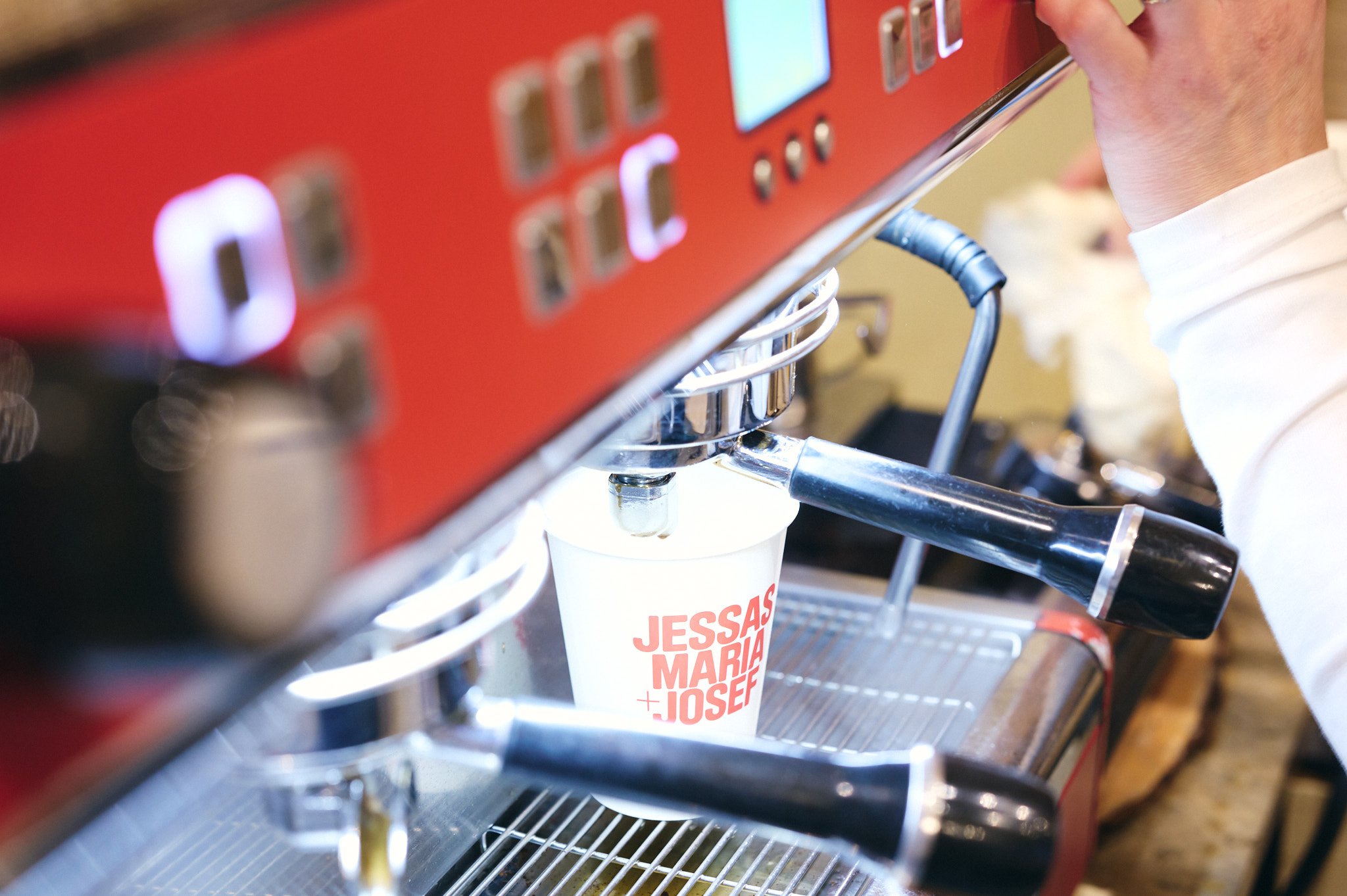 Eine Siebträgermaschine beim Brühen eines Kaffees in einer Tasse mit dem Schriftzug "JESSAS MARIA + JOSEF".
