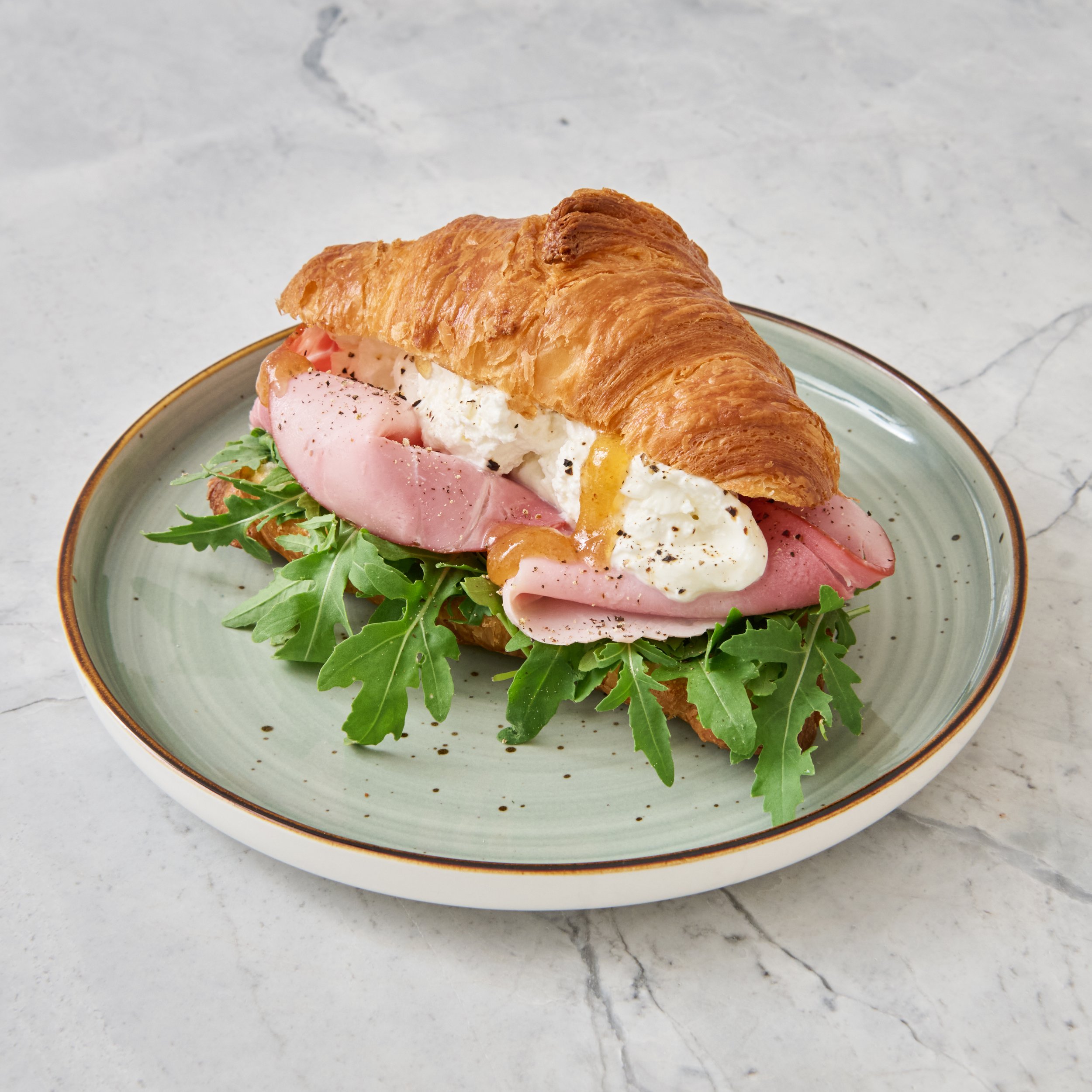 Ein Croissant mit Rucola, Schinken, Burrata und Feigensenf auf einem Teller.