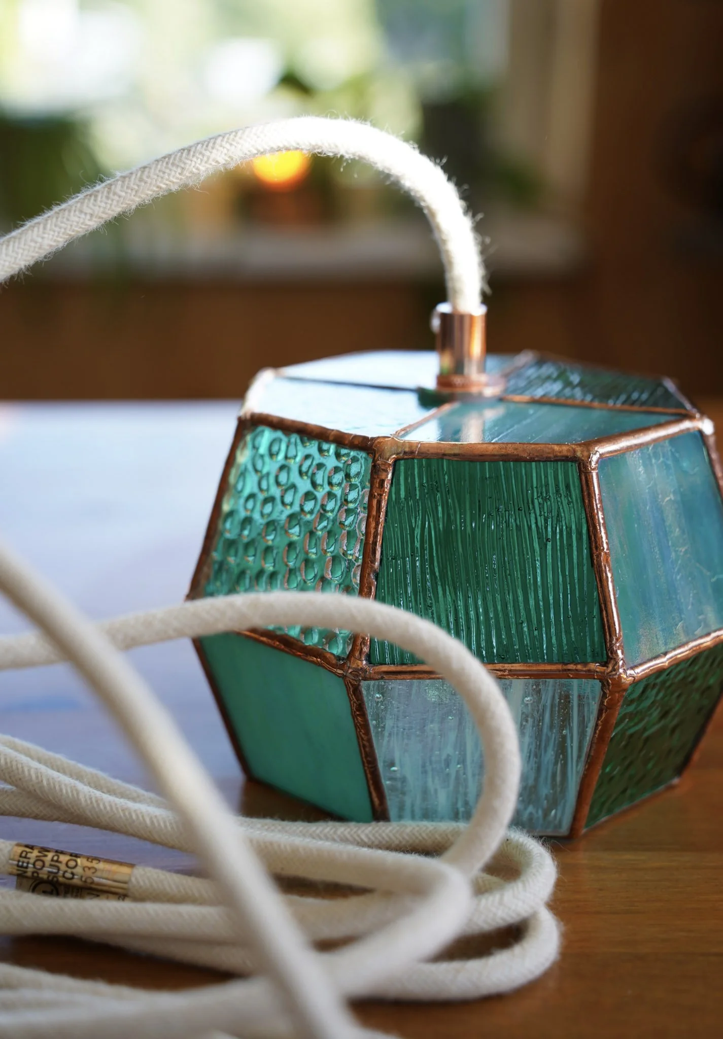 A decorative hanging lantern with a metallic geometric pattern and a lit candle inside, positioned next to a potted snake plant.