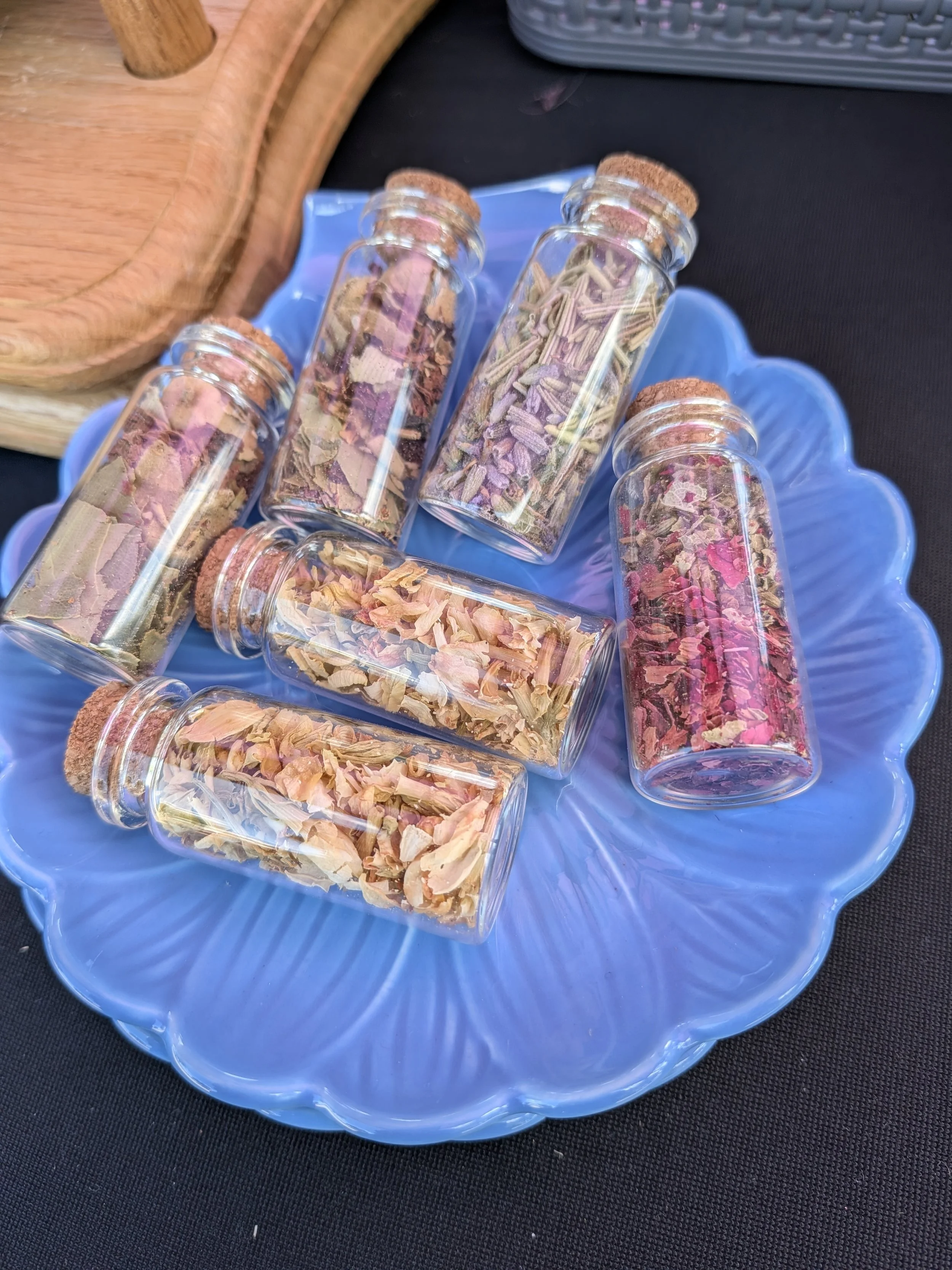 Small glass bottles filled with dried flower petals and herbs, arranged on a blue glass plate.