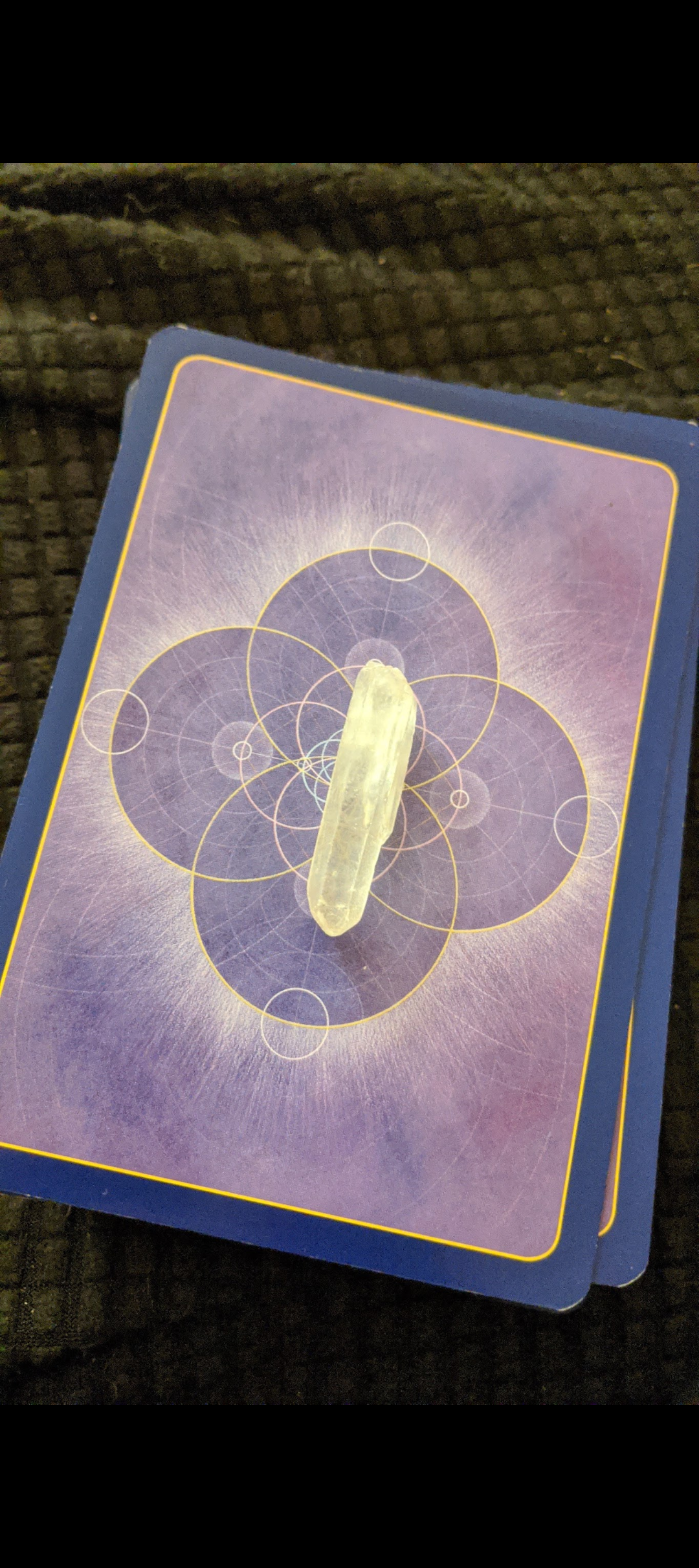 A tarot card with a purple background and geometric designs, featuring a clear quartz crystal placed on top.