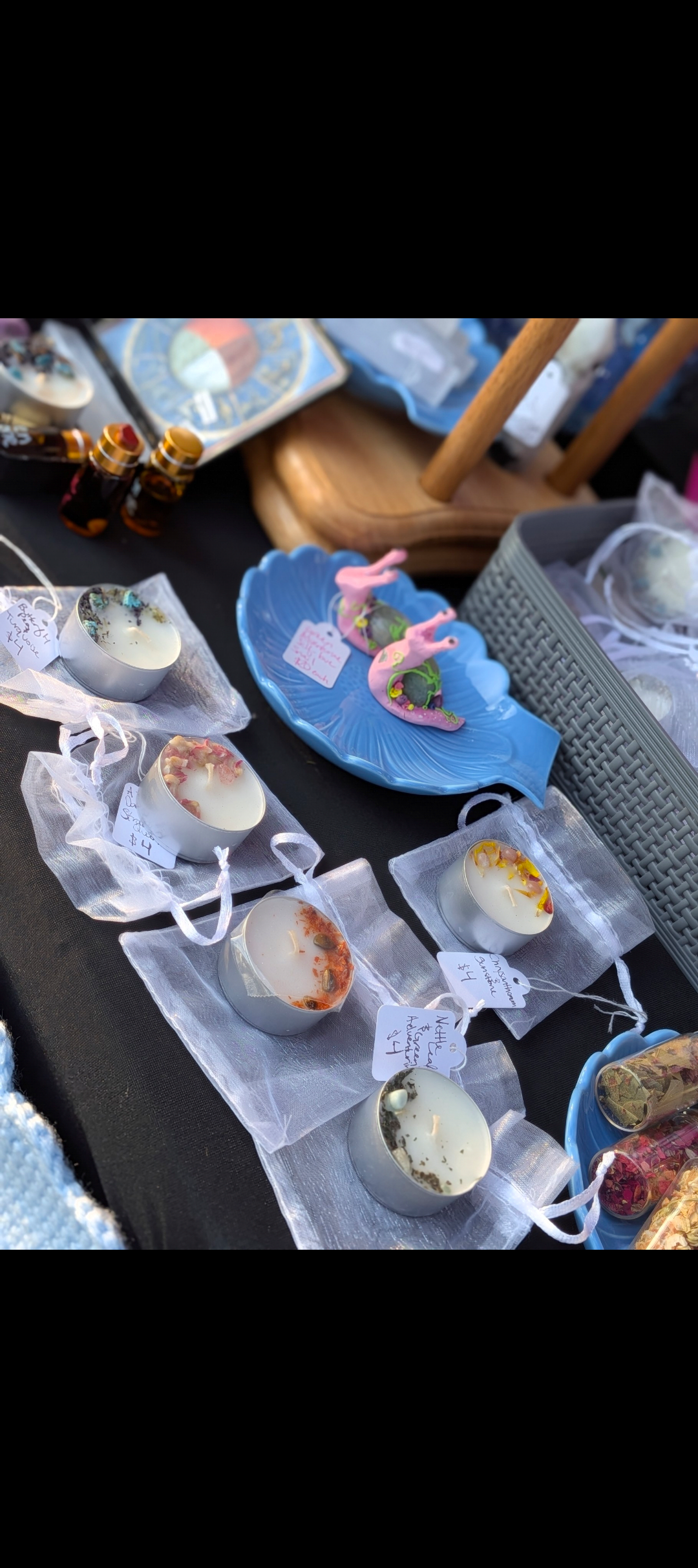 Display of various handmade candles and decorative items on a table at an outdoor market.