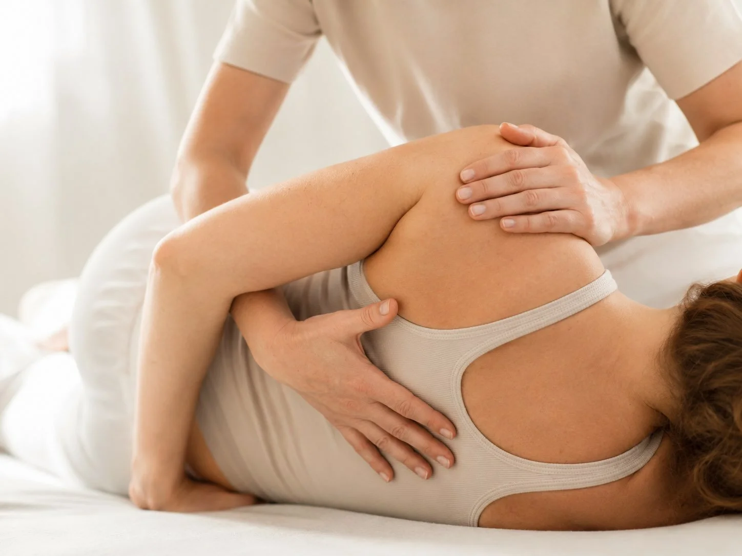 Eine Person liegt auf einer Seite im Bett, während eine andere Person eine physiotherapeutische Behandlung an ihrem Knie durchführt.