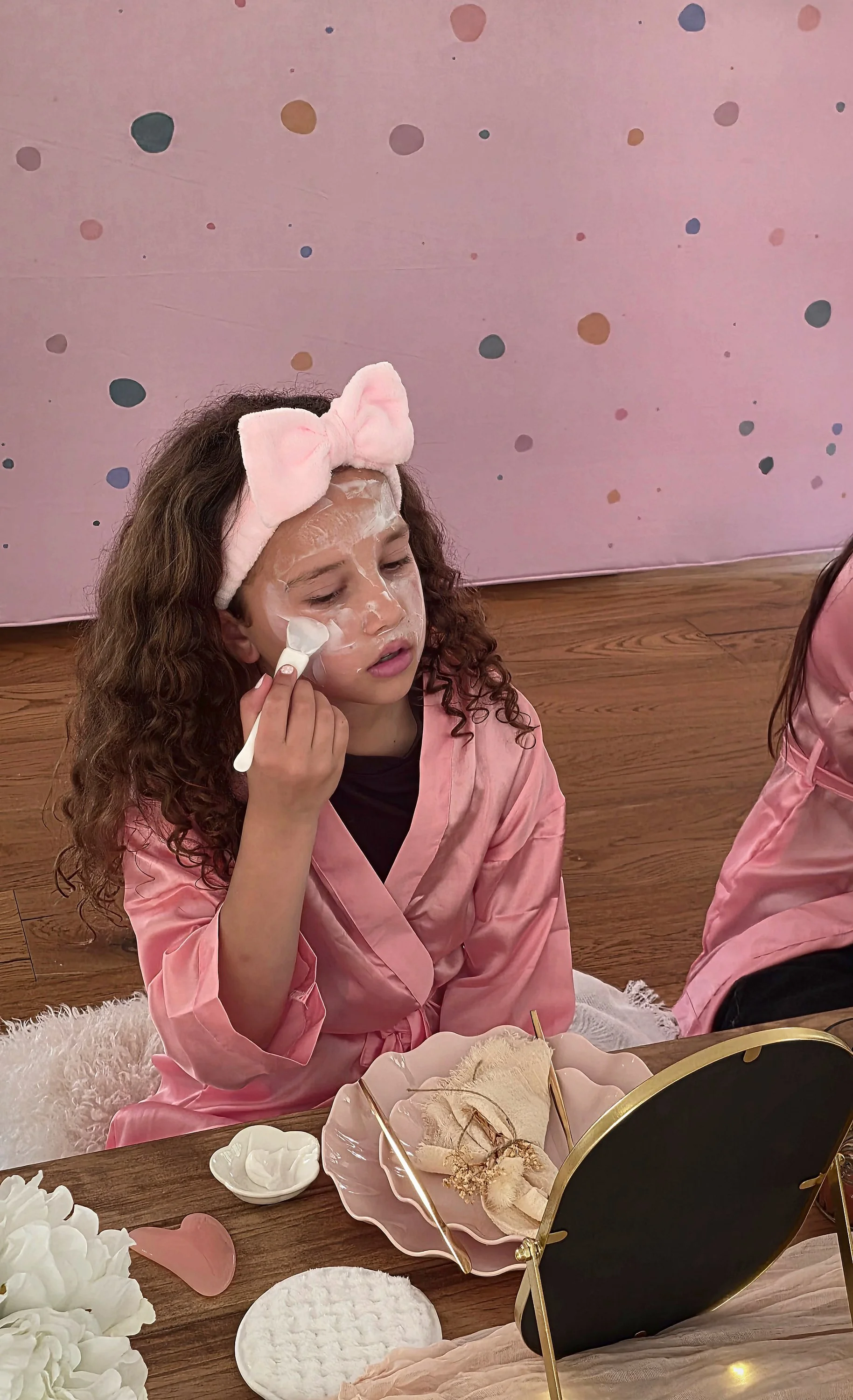 Girl in a pink robe brushing on a face mask during a spa party facial