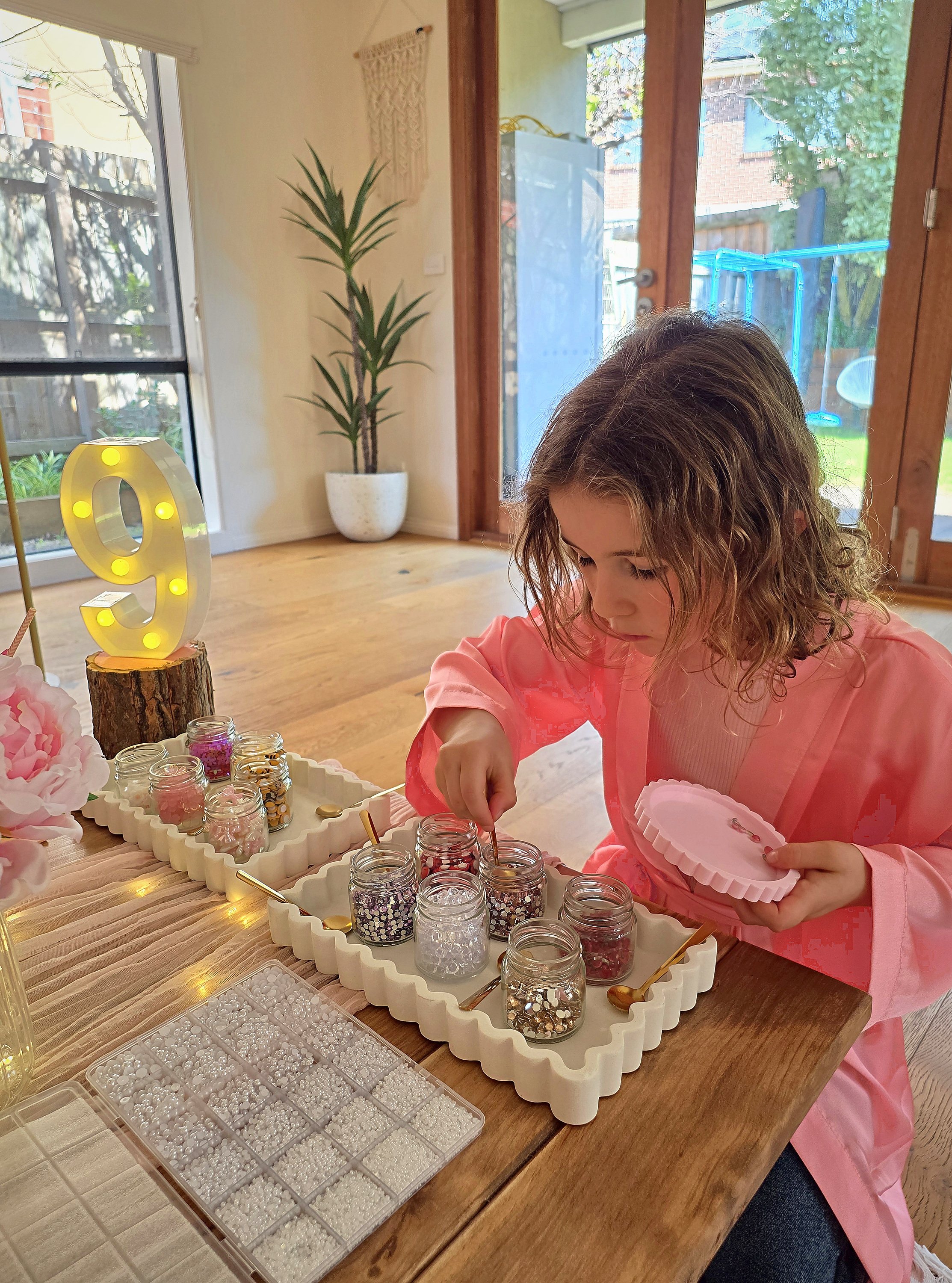 Girl in a pink robe choosing gems for claw clip decorating at the spa party table