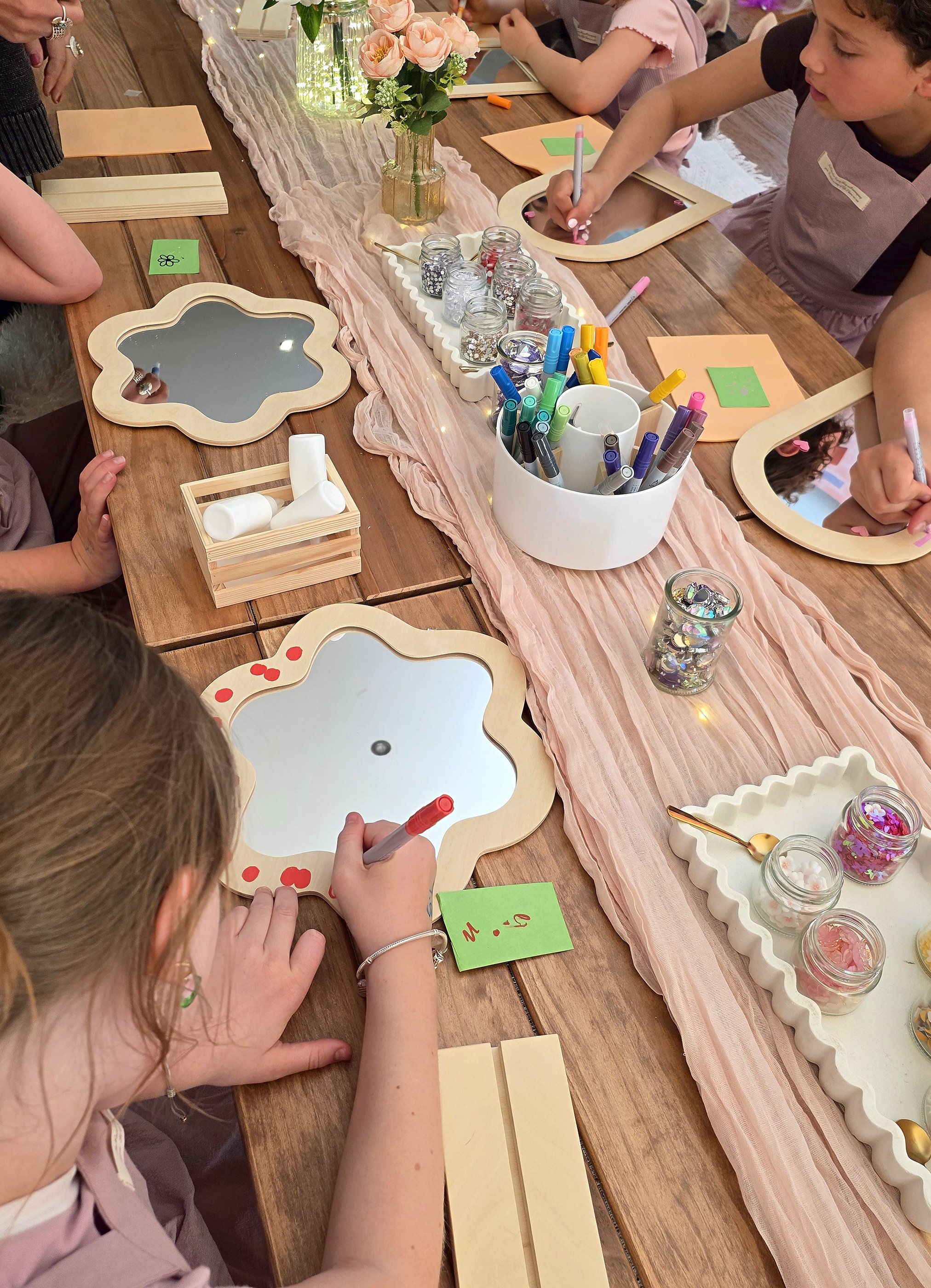 Overhead view of girls decorating flower-shaped mirrors around a long craft table