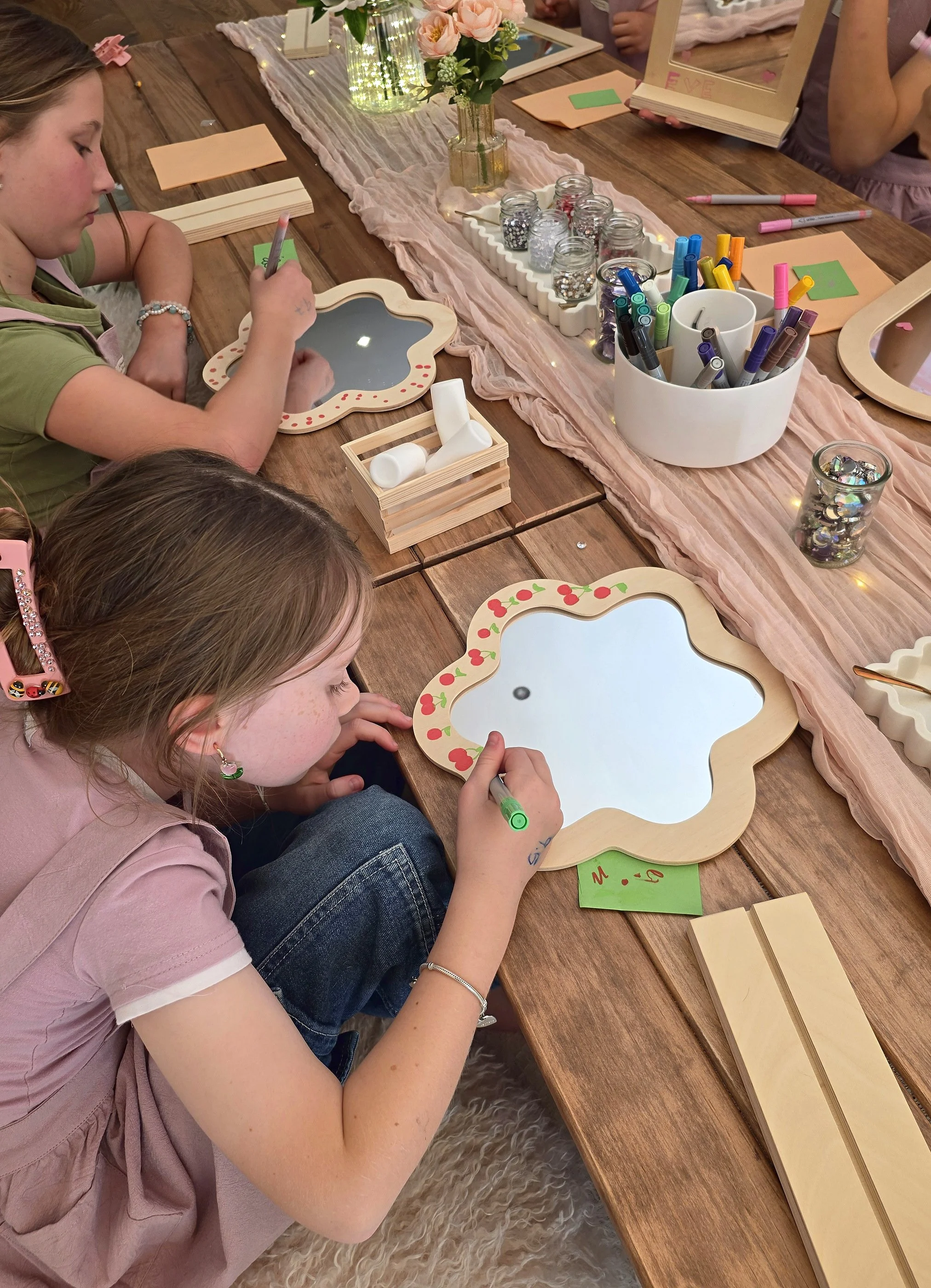 Girl painting colourful dots onto a flower-shaped wooden mirror at a craft party