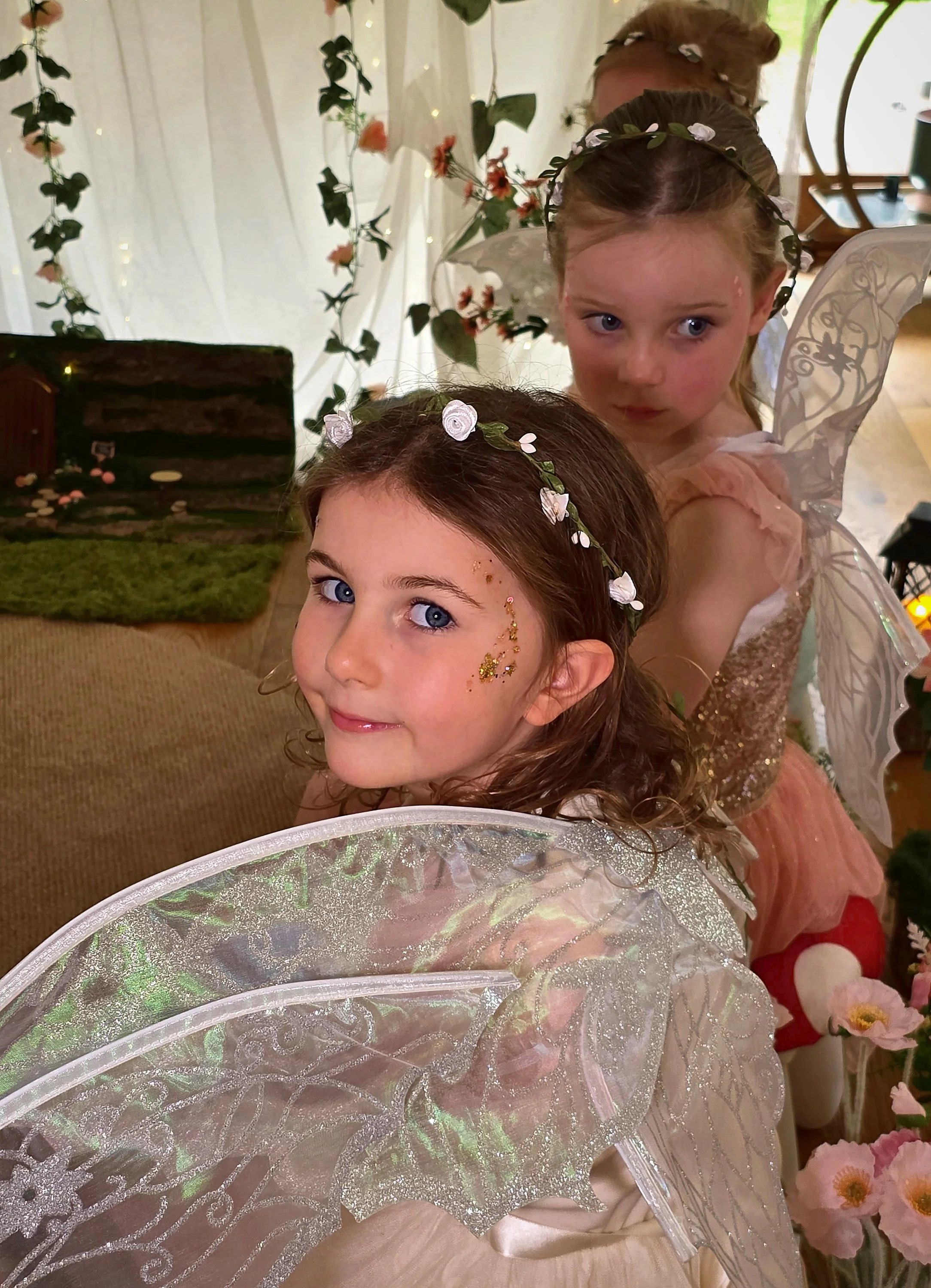 Little fairy with face gems and a flower crown smiling over her shoulder in her wings