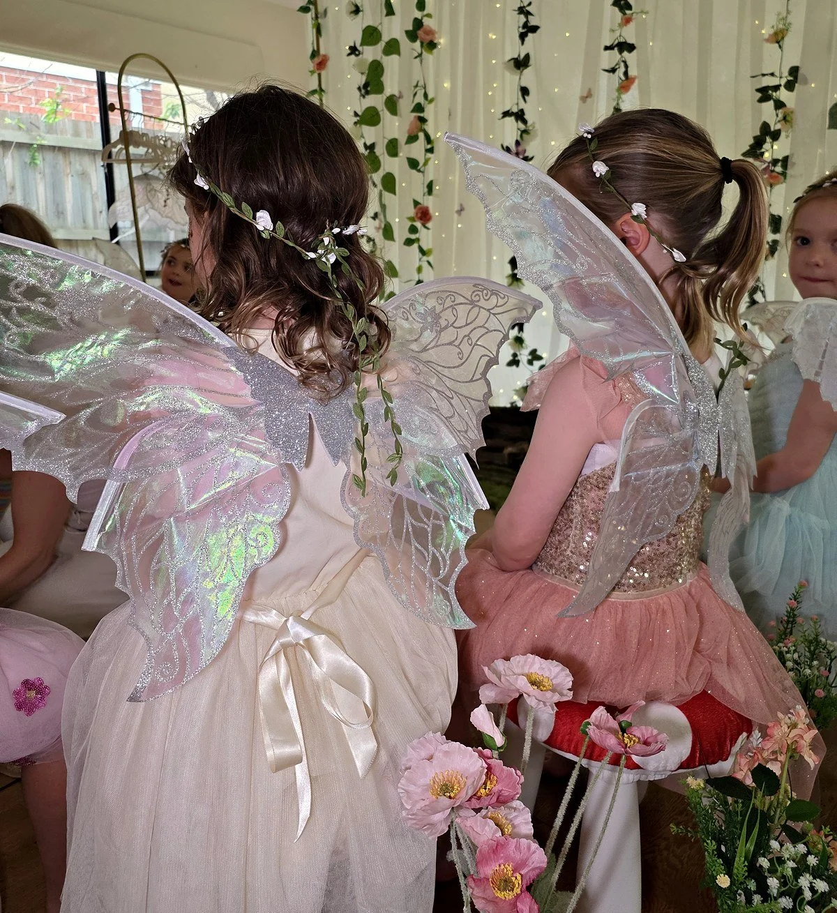 Two girls showing off iridescent fairy wings and flower crowns at an Enchanted Garden party