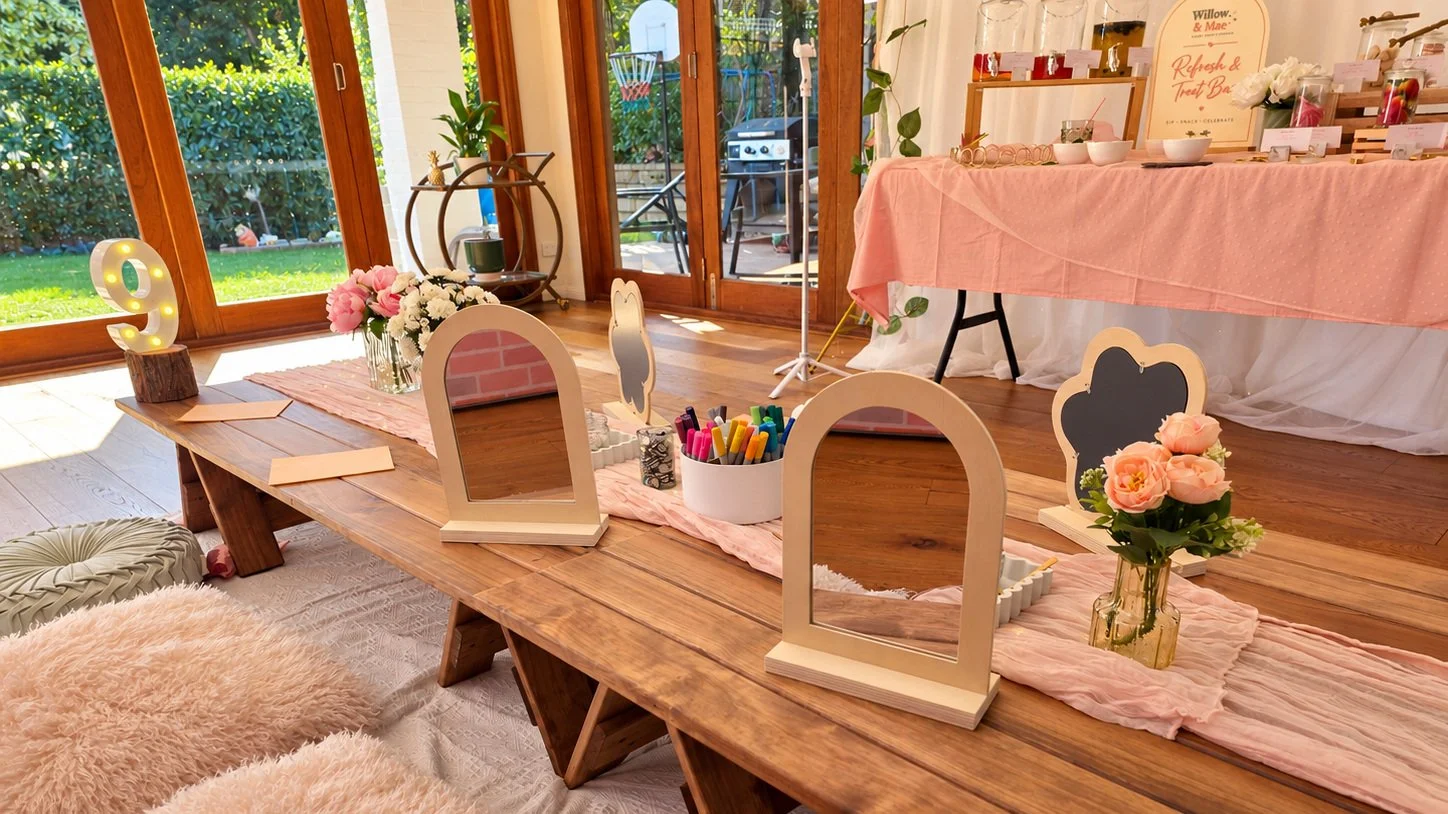 Craft party table set with wooden arched mirrors, paint pens and fresh roses, ready for guests