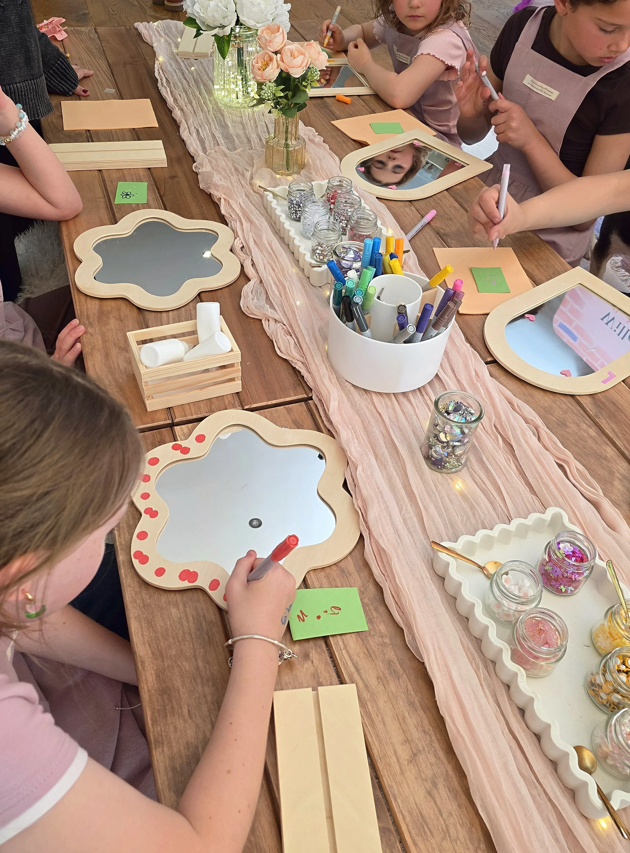 Child decorating a flower-shaped mirror with paint pens and gems