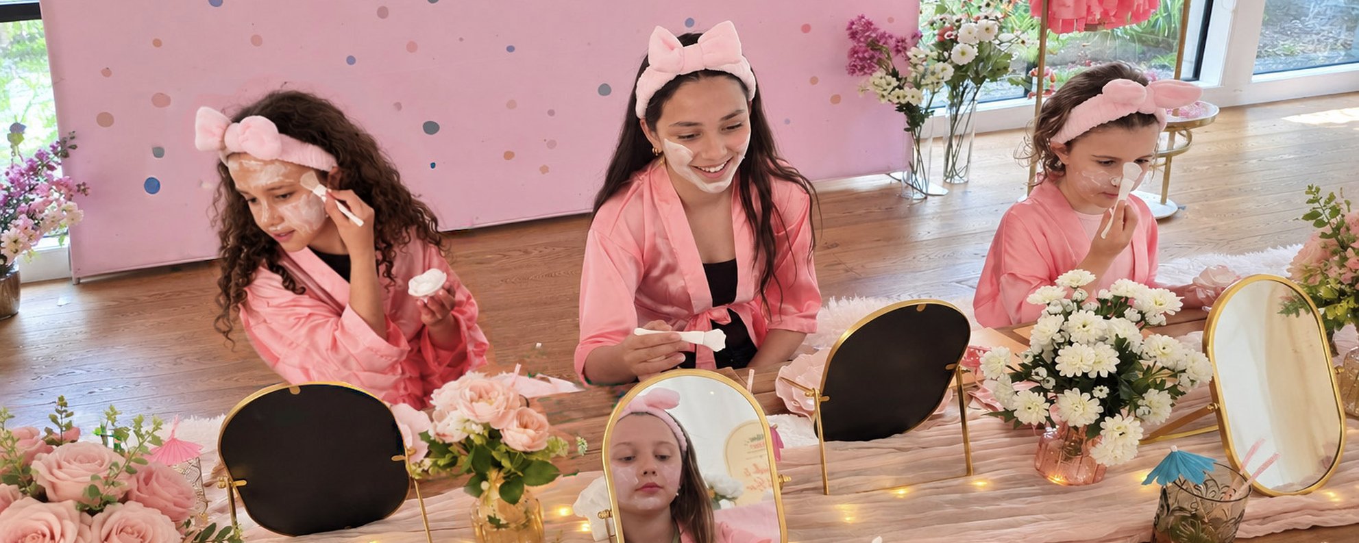 Girls in pink robes and bow headbands doing face masks at a Spa Retreat party
