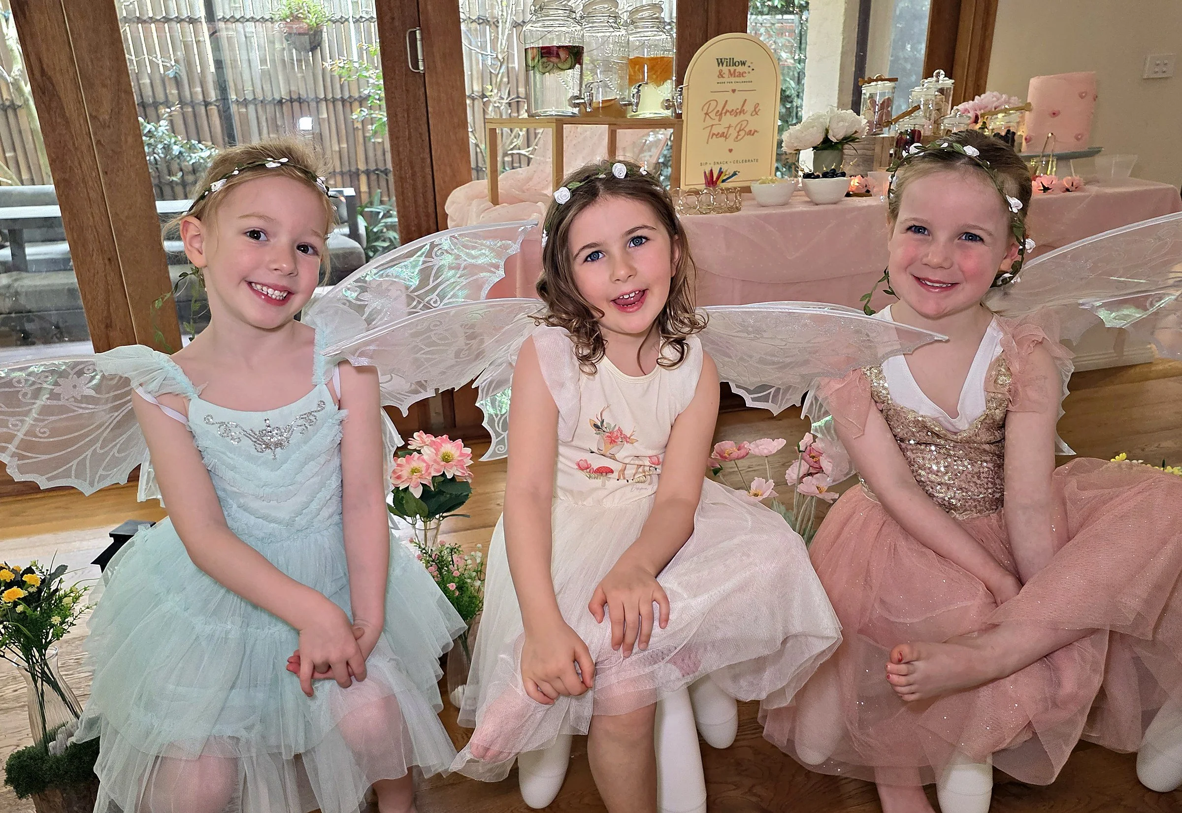 Three smiling girls in fairy wings and flower crowns at an at-home Enchanted Garden fairy party in Melbourne