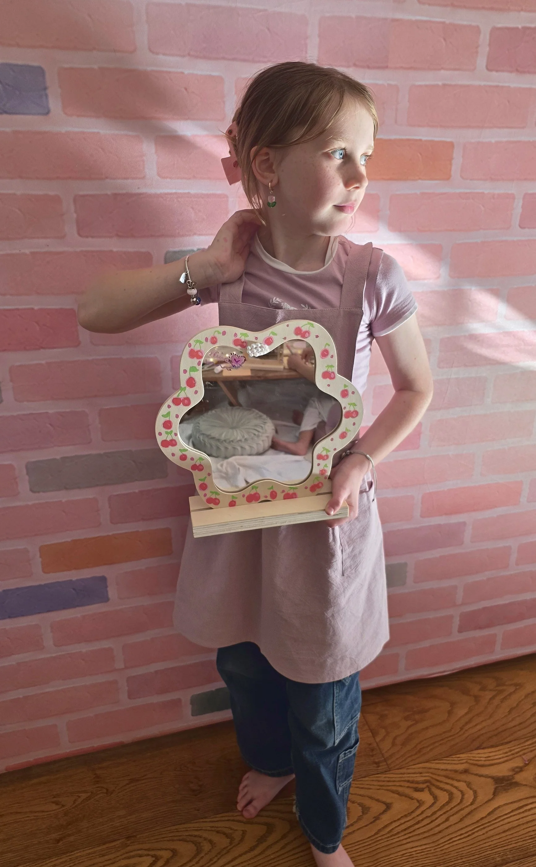 Proud girl in a craft apron holding the flower mirror she decorated at her Creative Studio party
