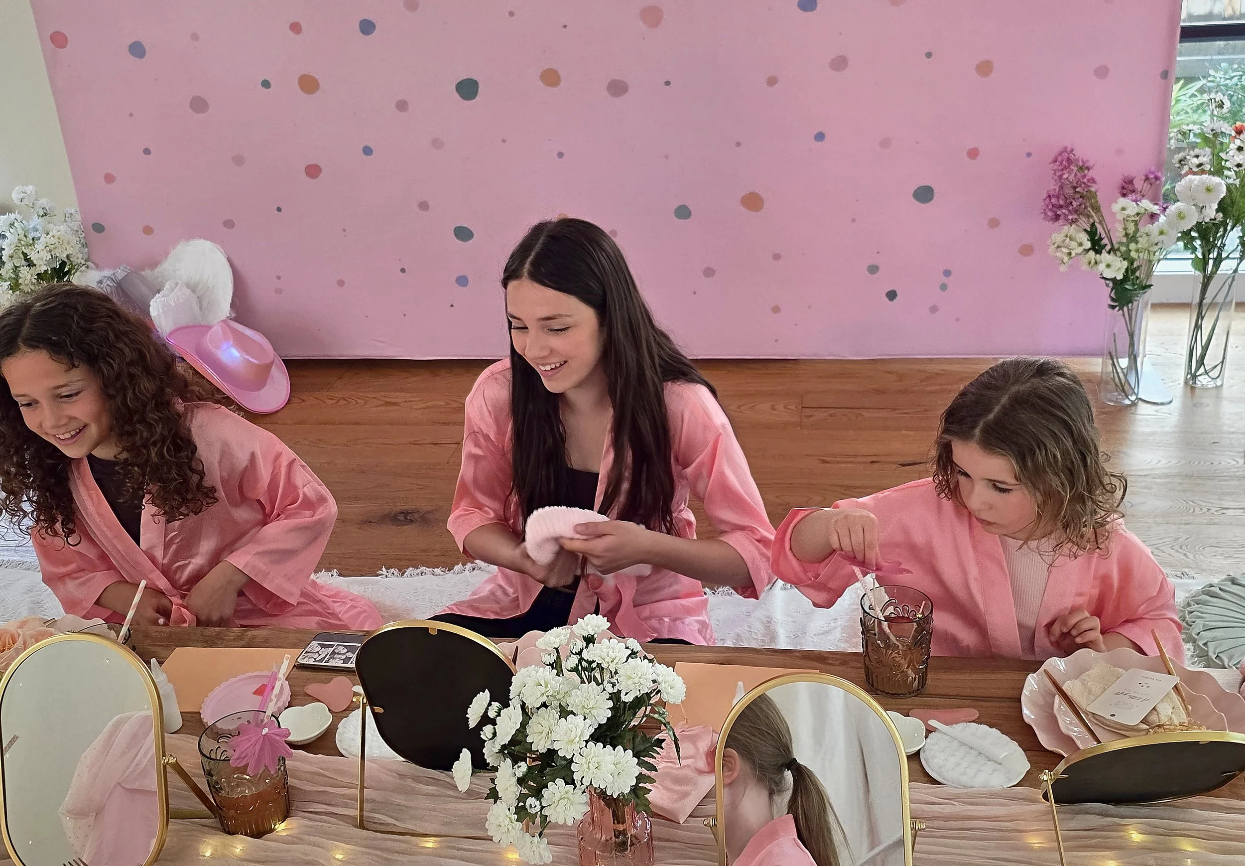 Three girls laughing in pink robes while doing face masks at a spa party