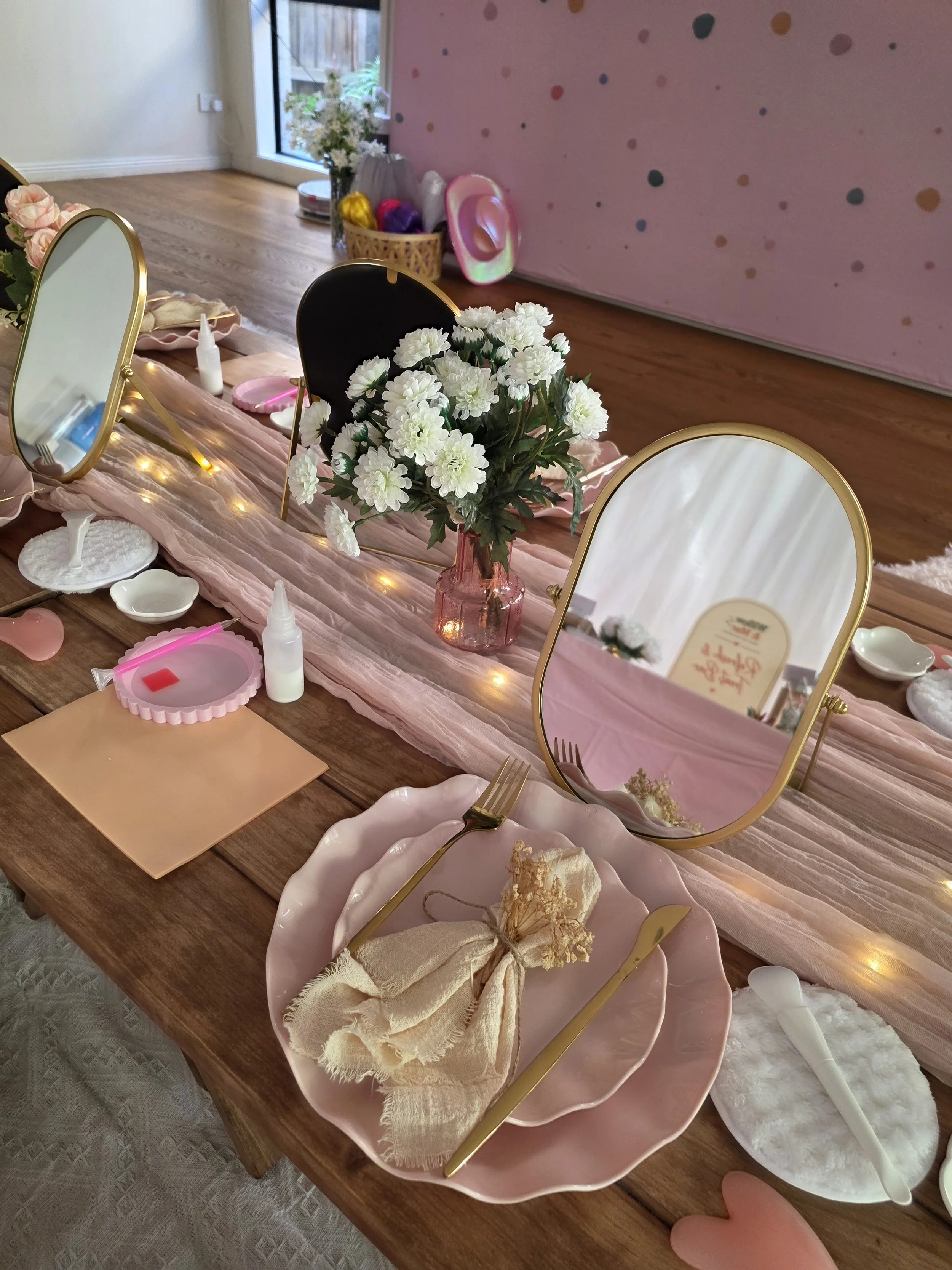 Pamper station with a gold oval mirror, pink plate and white flowers at a girls' spa party
