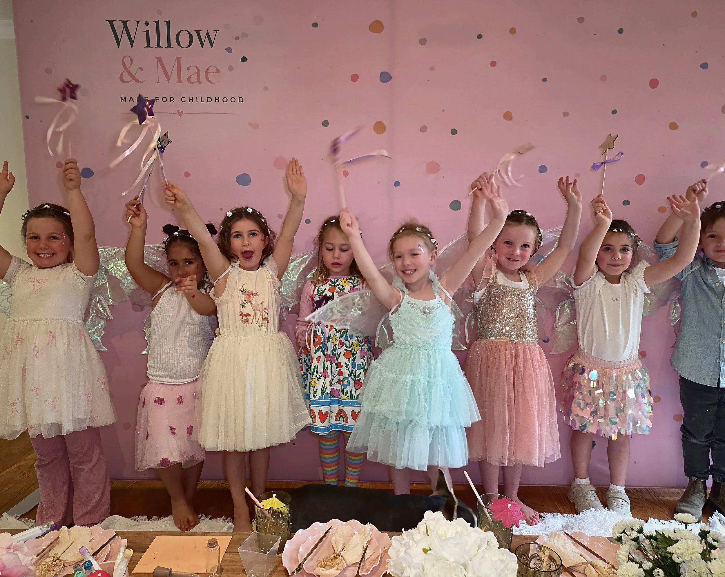 Fairy party guests cheering with their wands in front of the Willow & Mae backdrop