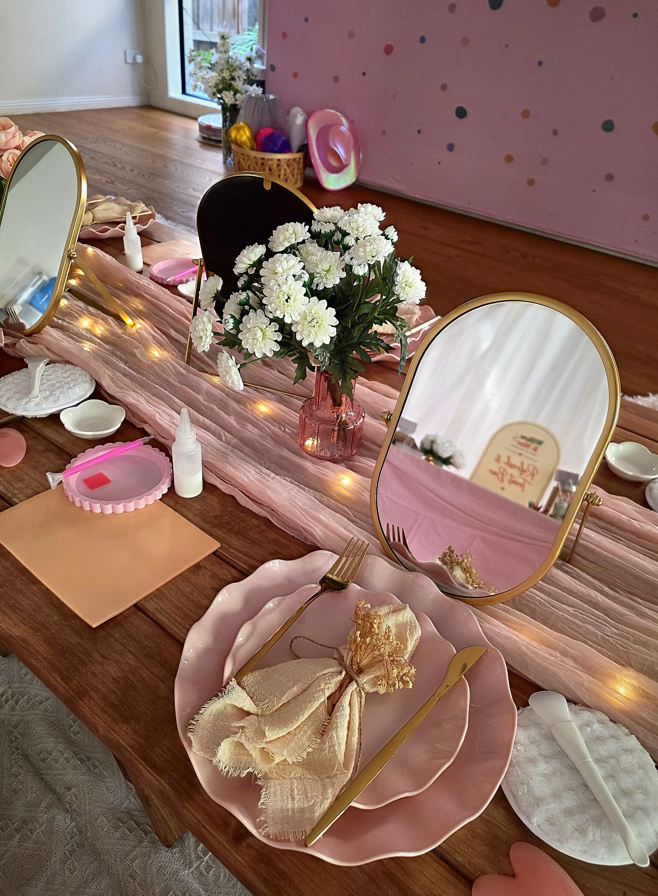 Spa party place setting with a gold mirror, scalloped pink plate, satin bow and fairy lights