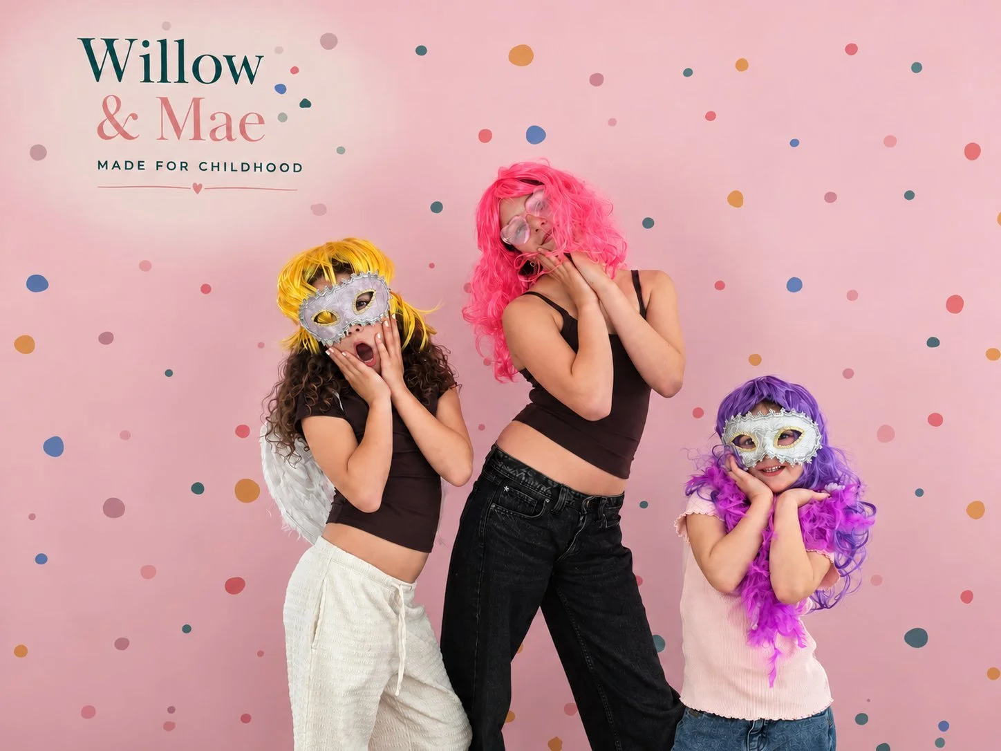 Friends in bright wigs and sparkly masks striking a pose at the party photo backdrop