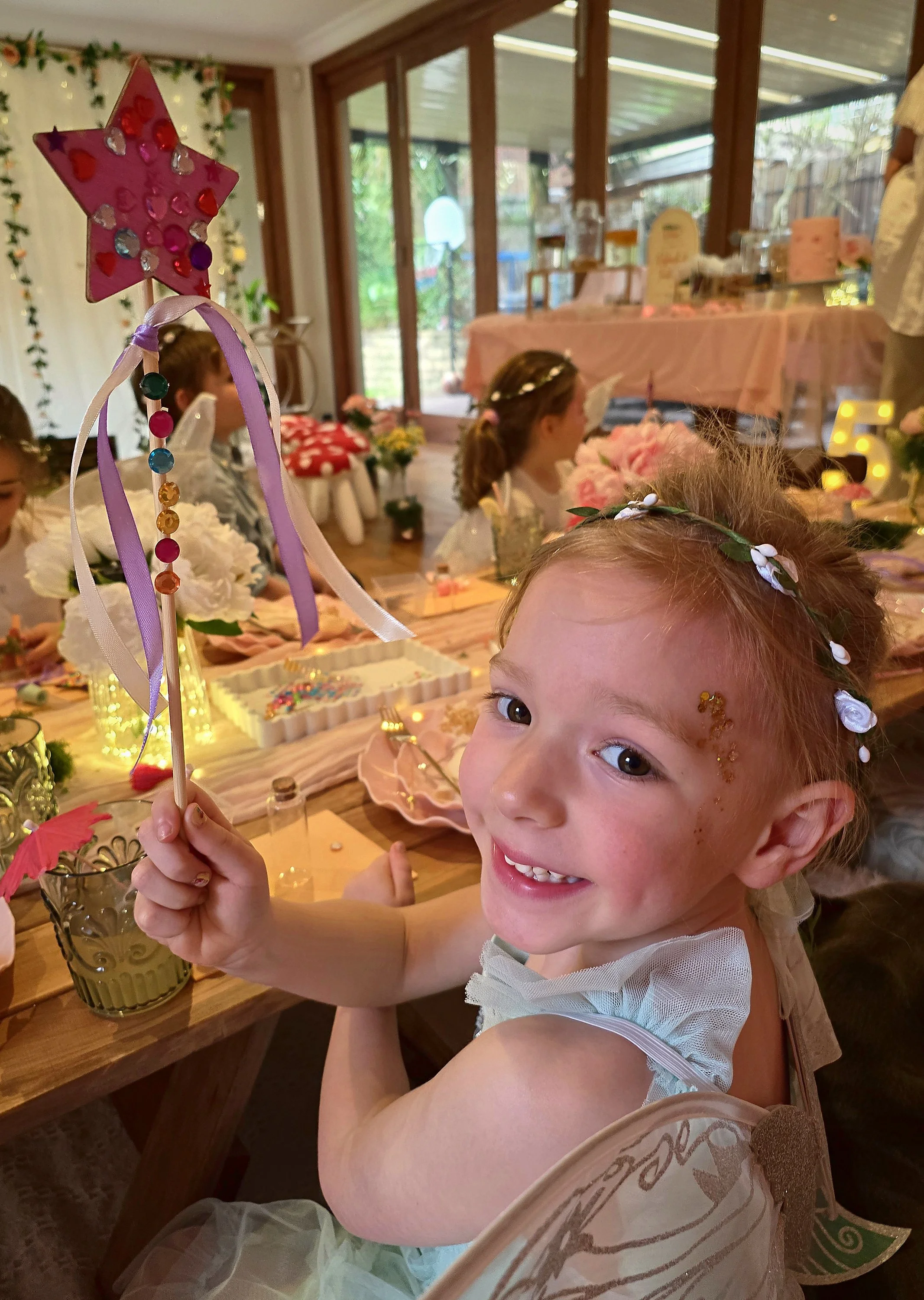 Beaming girl holding up the sparkly star wand she made at her fairy party