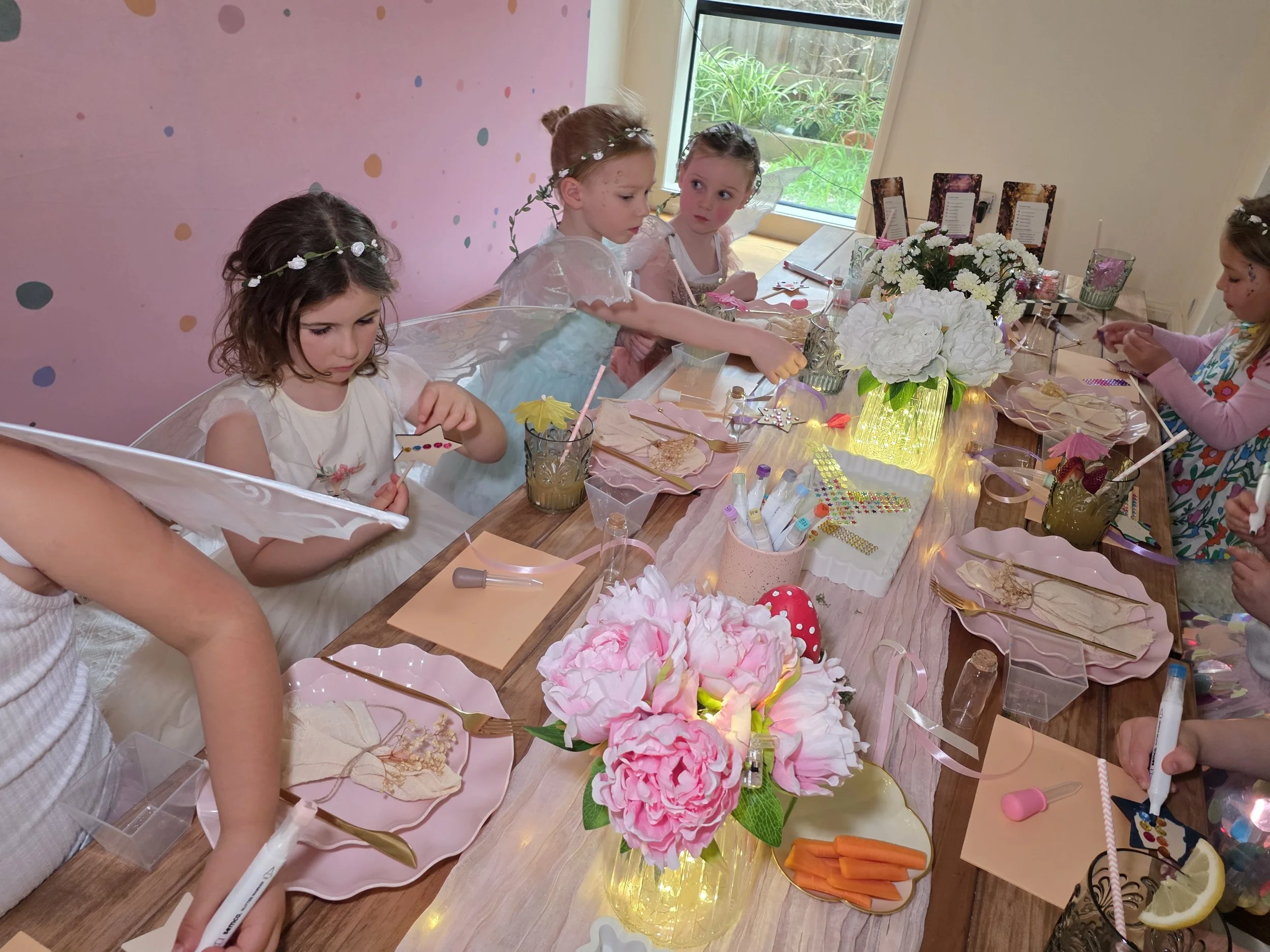Little fairies decorating wands at a table with pink peonies and fairy lights