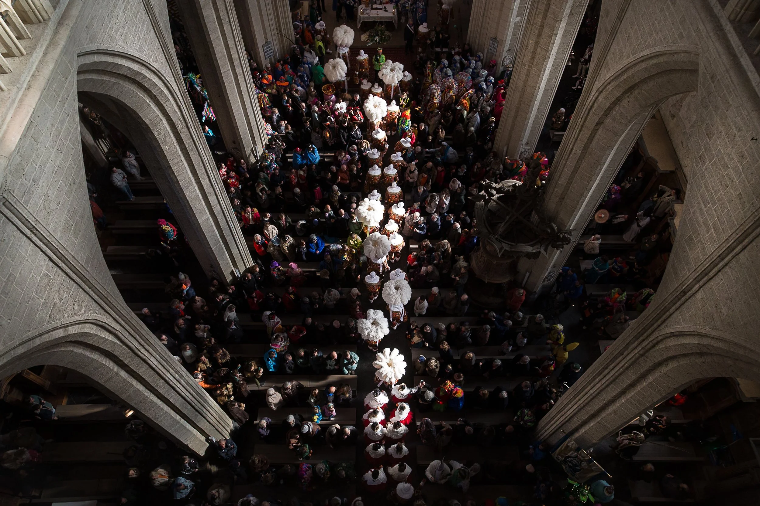 Une foule de personnes dans une église ou une cathédrale, semblent participer à une cérémonie ou un événement religieux, avec une décoration florale et des lampes suspendues.