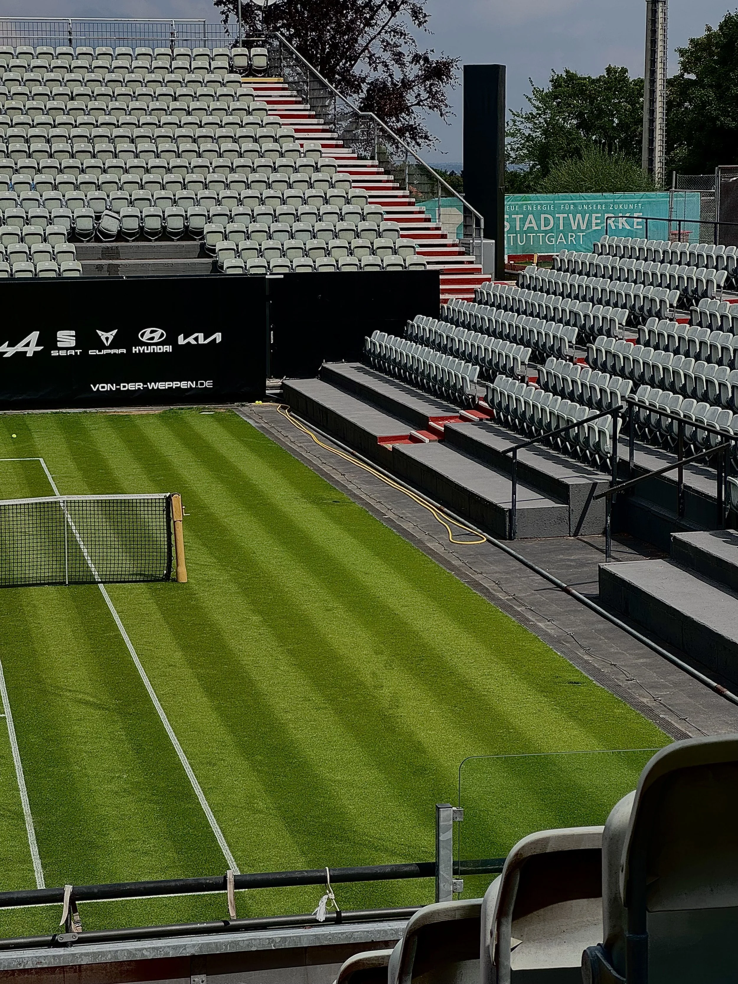 Empty stadium stands with black and grey chairs and green soccer field in foreground.