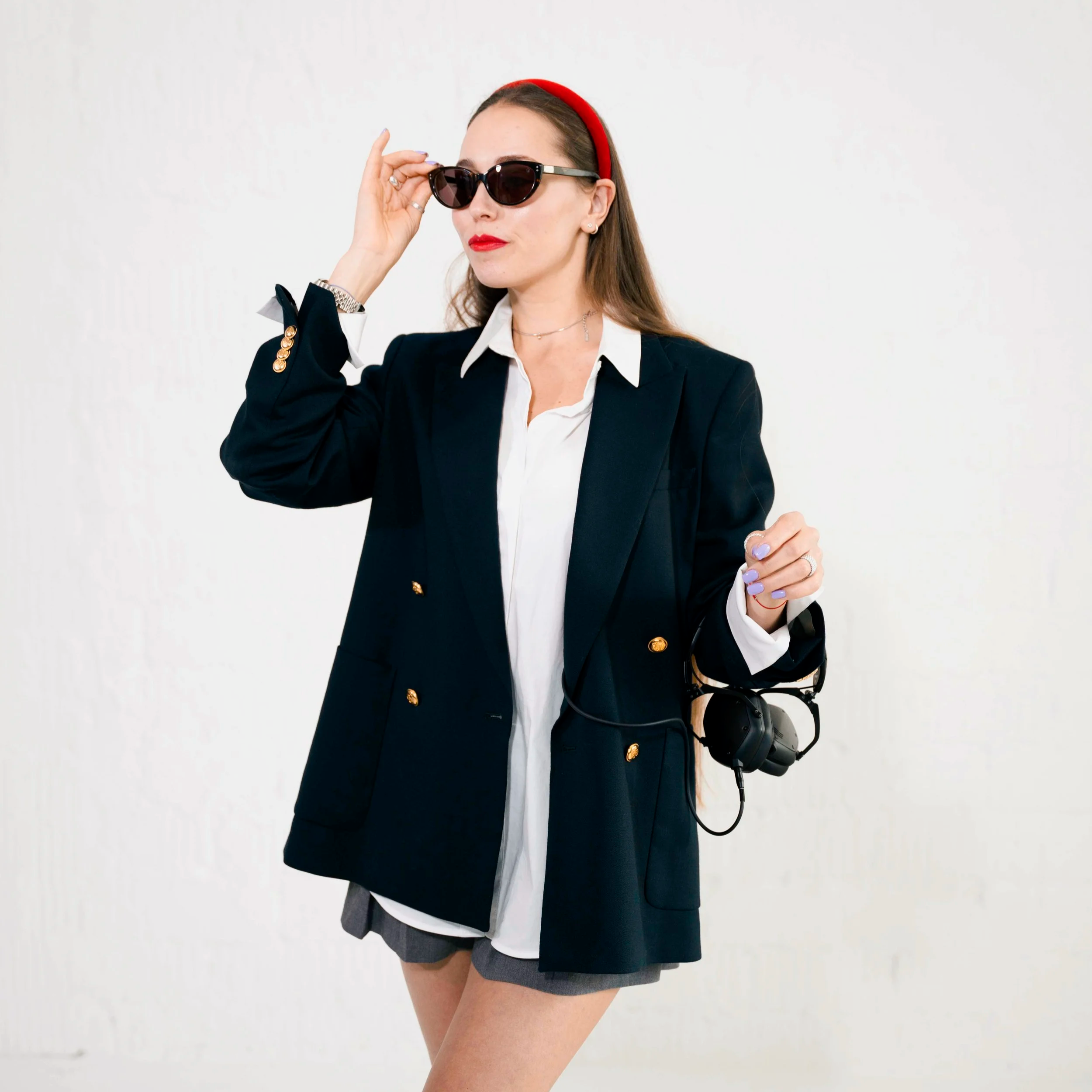 A woman dressed in business attire wearing sunglasses and a red headband, holding a camera in her handbag.