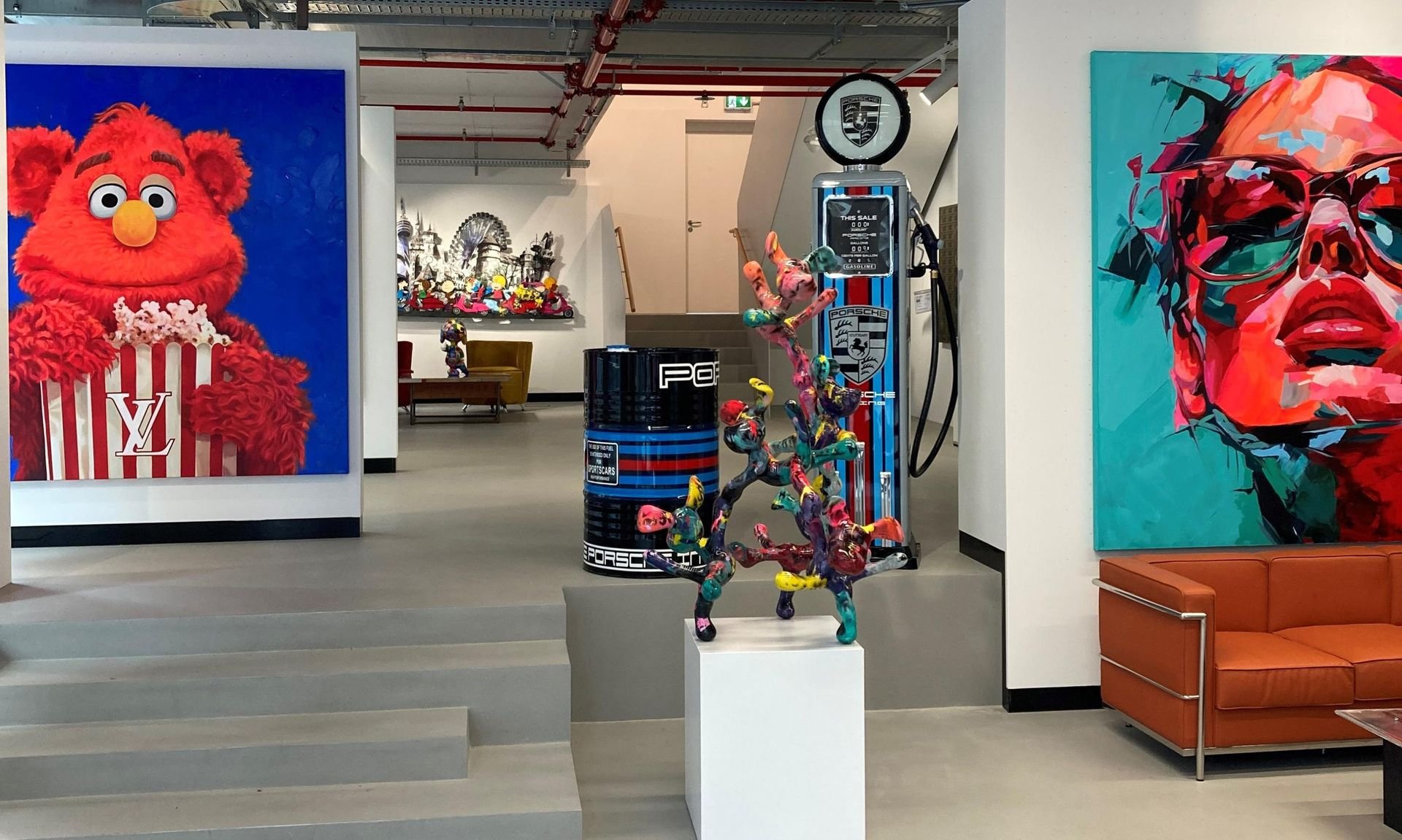 Interior of an art gallery with colorful paintings, sculptures, and a vintage gas pump. The left side features a vibrant painting of a furry red character with a popcorn box, and the right side shows a stylized portrait of a person with sunglasses. Bright artworks and modern sculpture are displayed throughout the space.