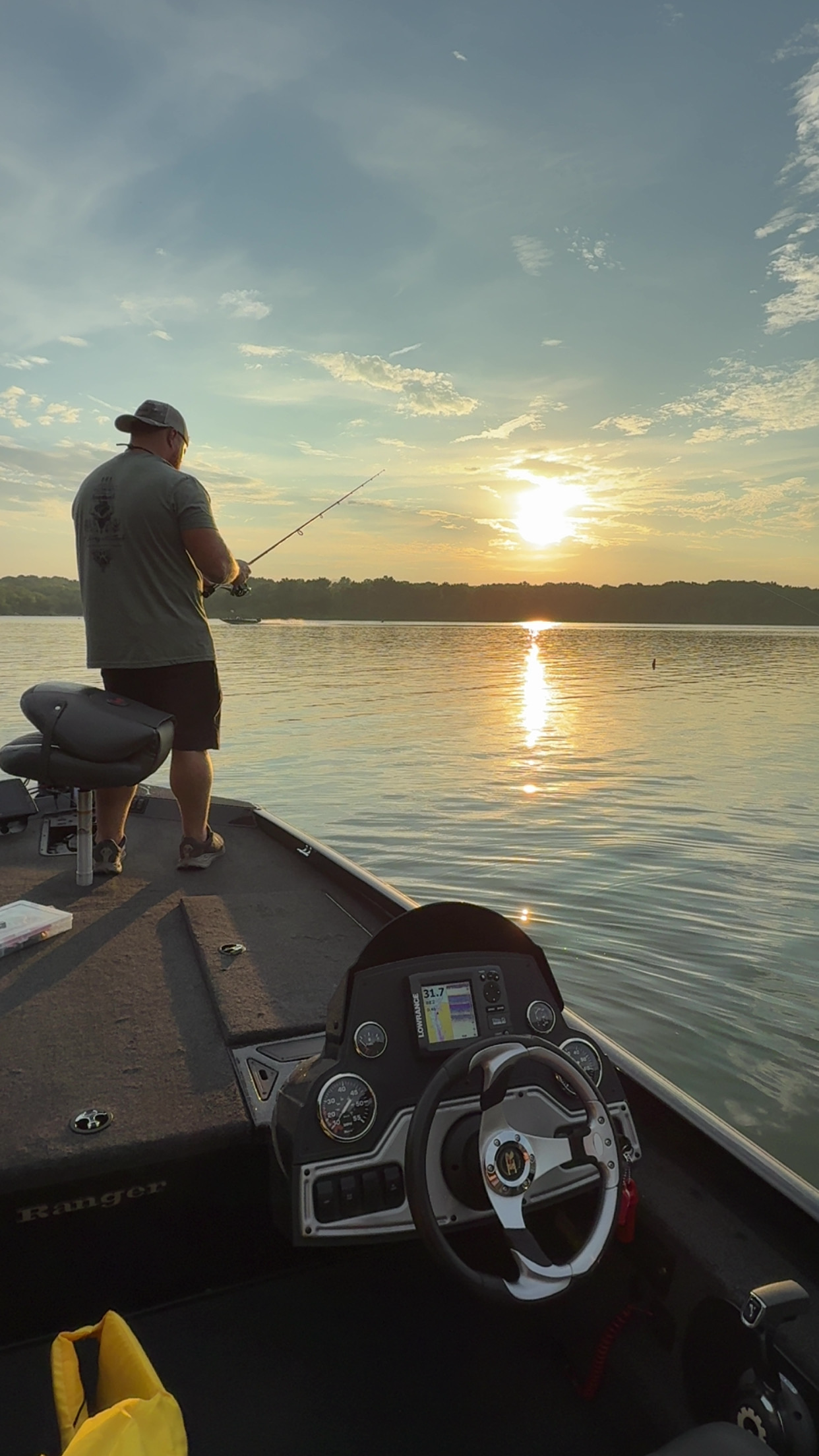 A person fishing from a boat during sunset on a calm lake, with a fish finder device visible on the boat's dashboard.