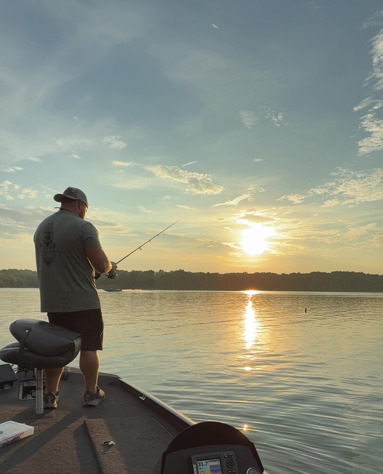 A man fishing from a boat on a lake during sunset.