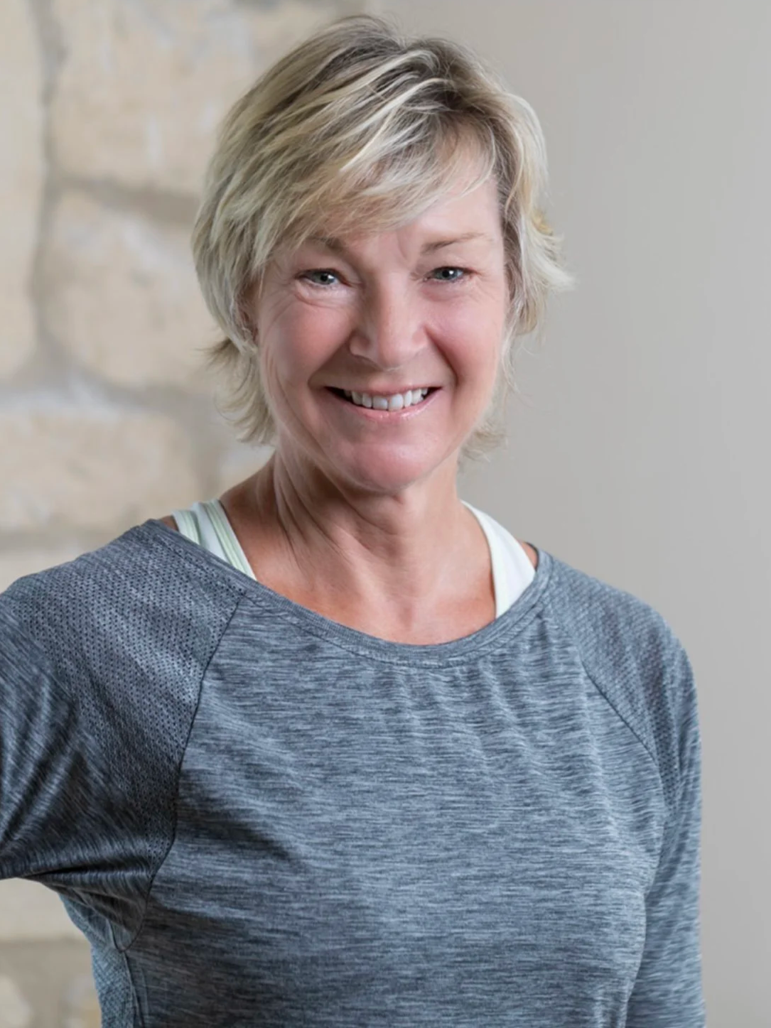 A smiling woman with short blonde hair wearing a gray athletic shirt.