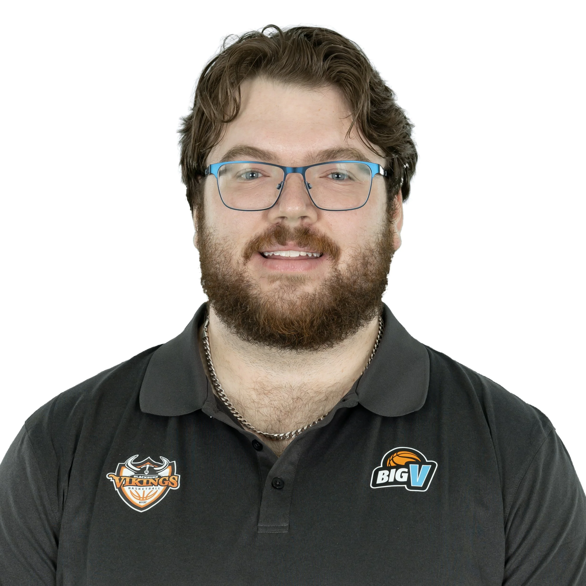 Close-up of a young man with brown hair and a beard, wearing blue-rimmed glasses and a black sports jersey with logos, smiling at the camera.