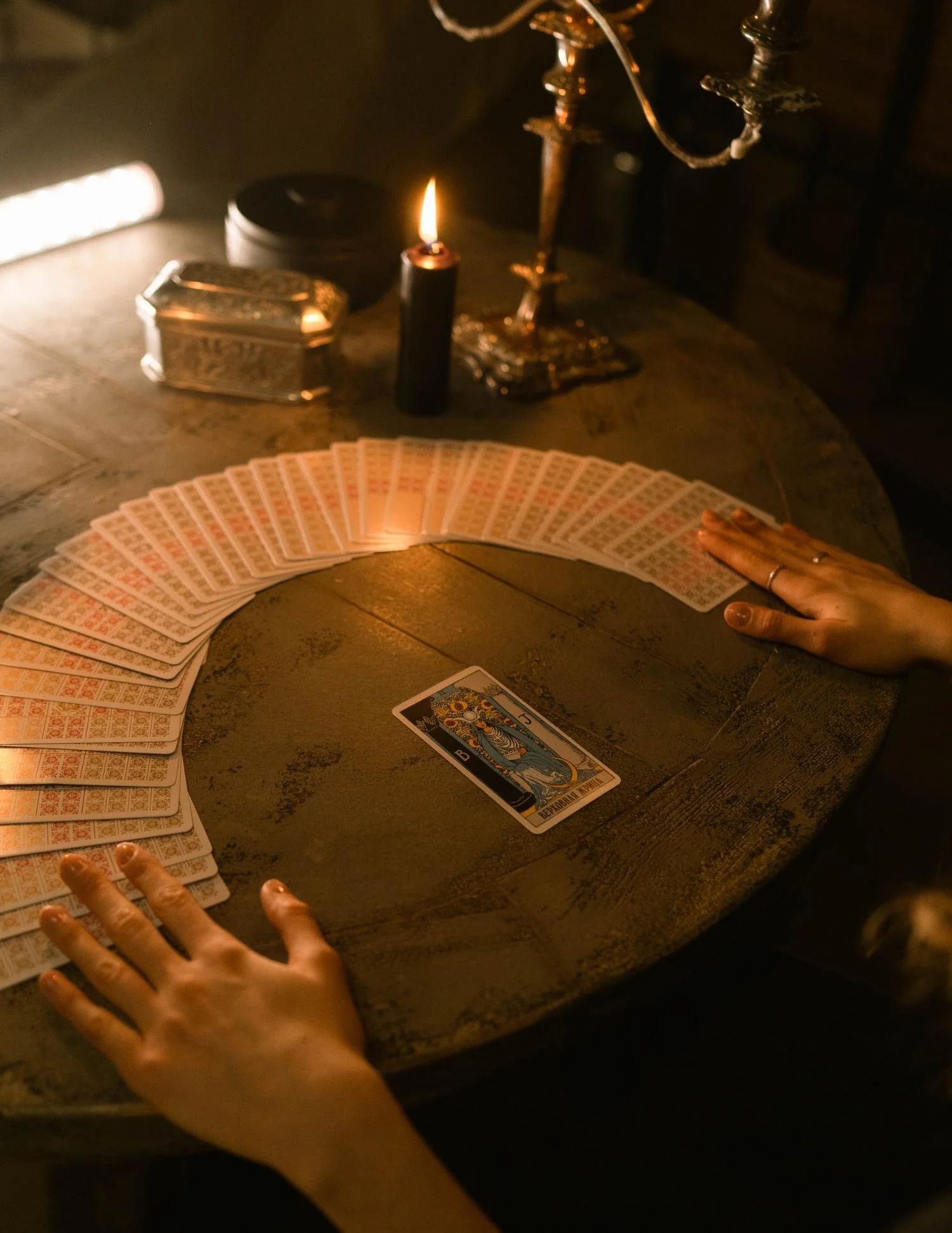 Happy tarot card reader with a spread of tarot cards on a wooden table, lit by a candle and vintage jewelry.